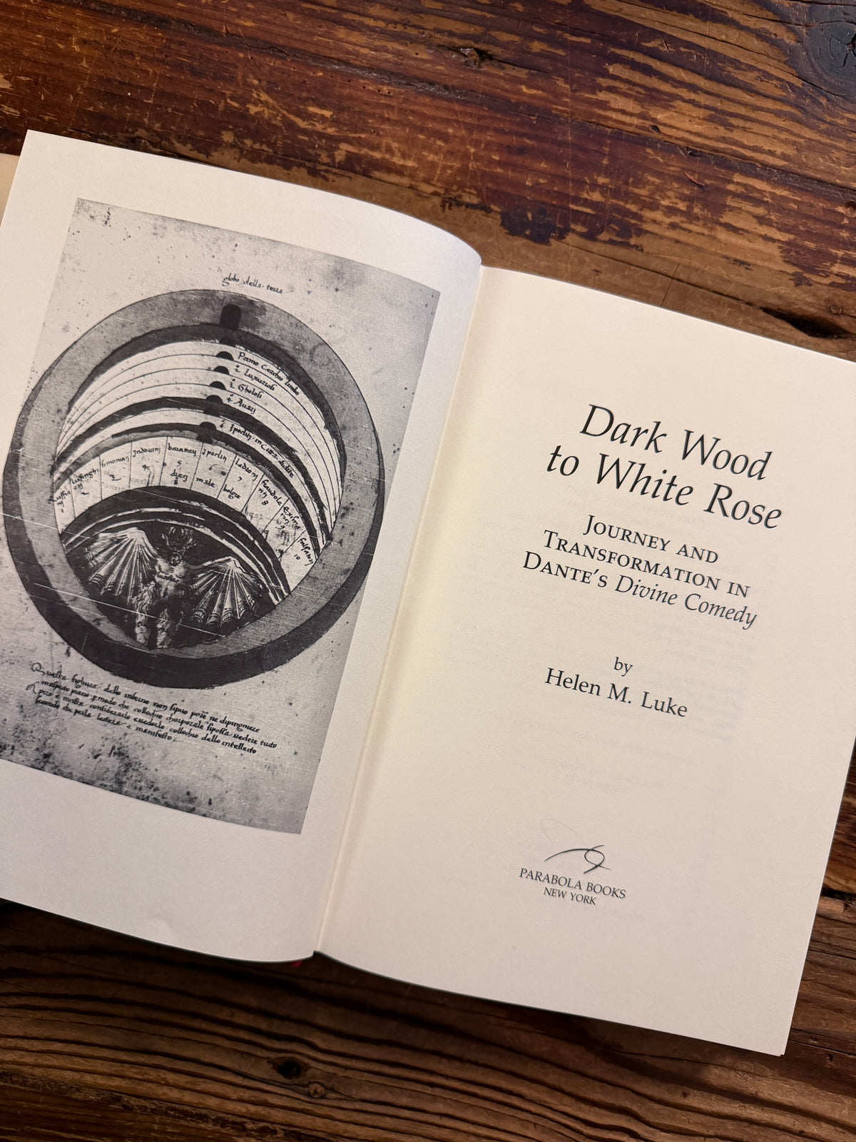 Open book on the title page of a book with the title 'Dark Wood to White Rose, journey and transformation in Dante’s Divine Comedy' by Helen M. Luke on a wooden surface 