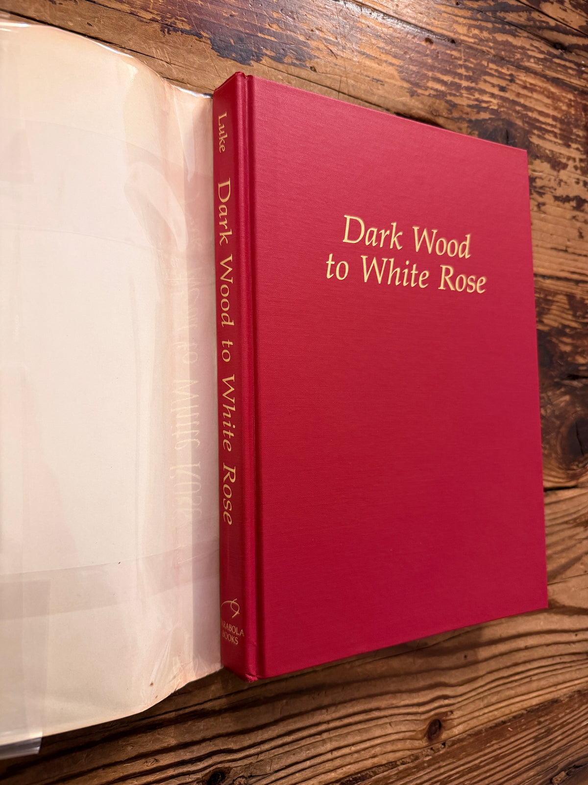 Front cover and spine without the dust jacket of a book with the title 'Dark Wood to White Rose, journey and transformation in Dante’s Divine Comedy' by Helen M. Luke on a wooden surface 