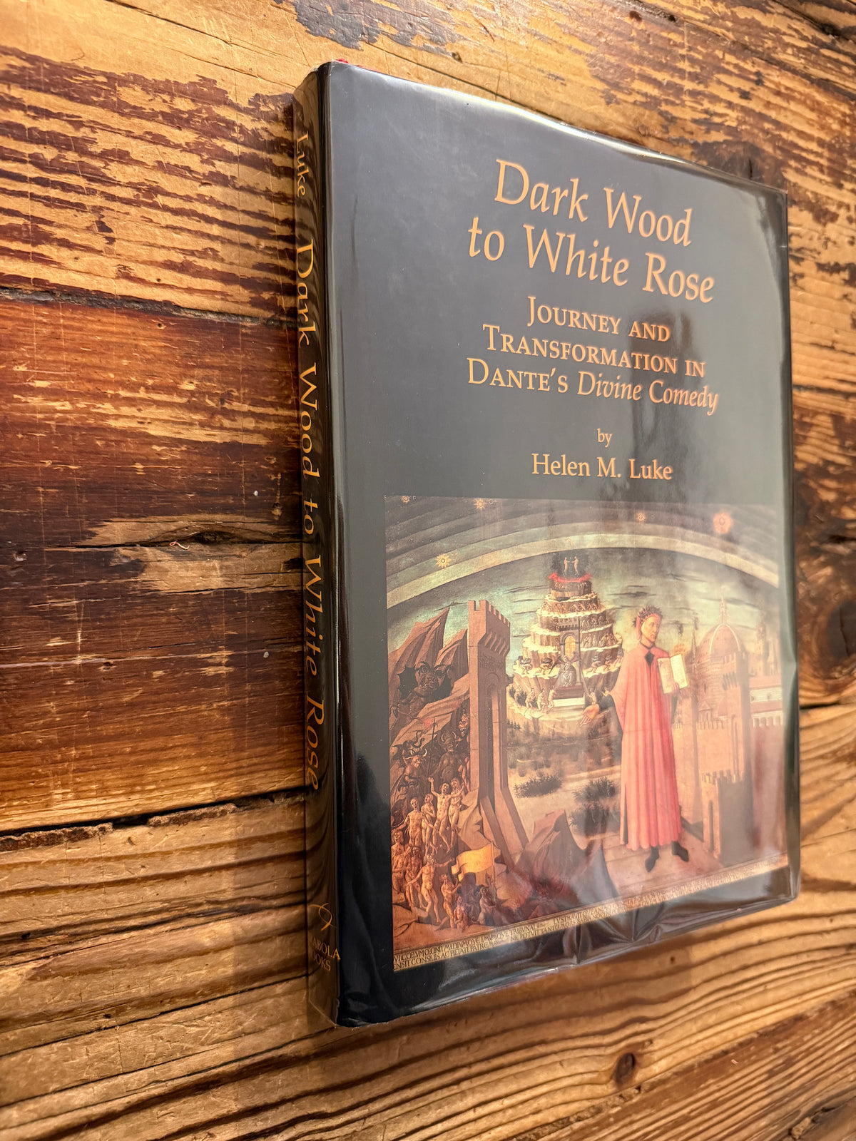 Front cover and spine of a book with the title 'Dark Wood to White Rose, journey and transformation in Dante’s Divine Comedy' by Helen M. Luke on a wooden surface 