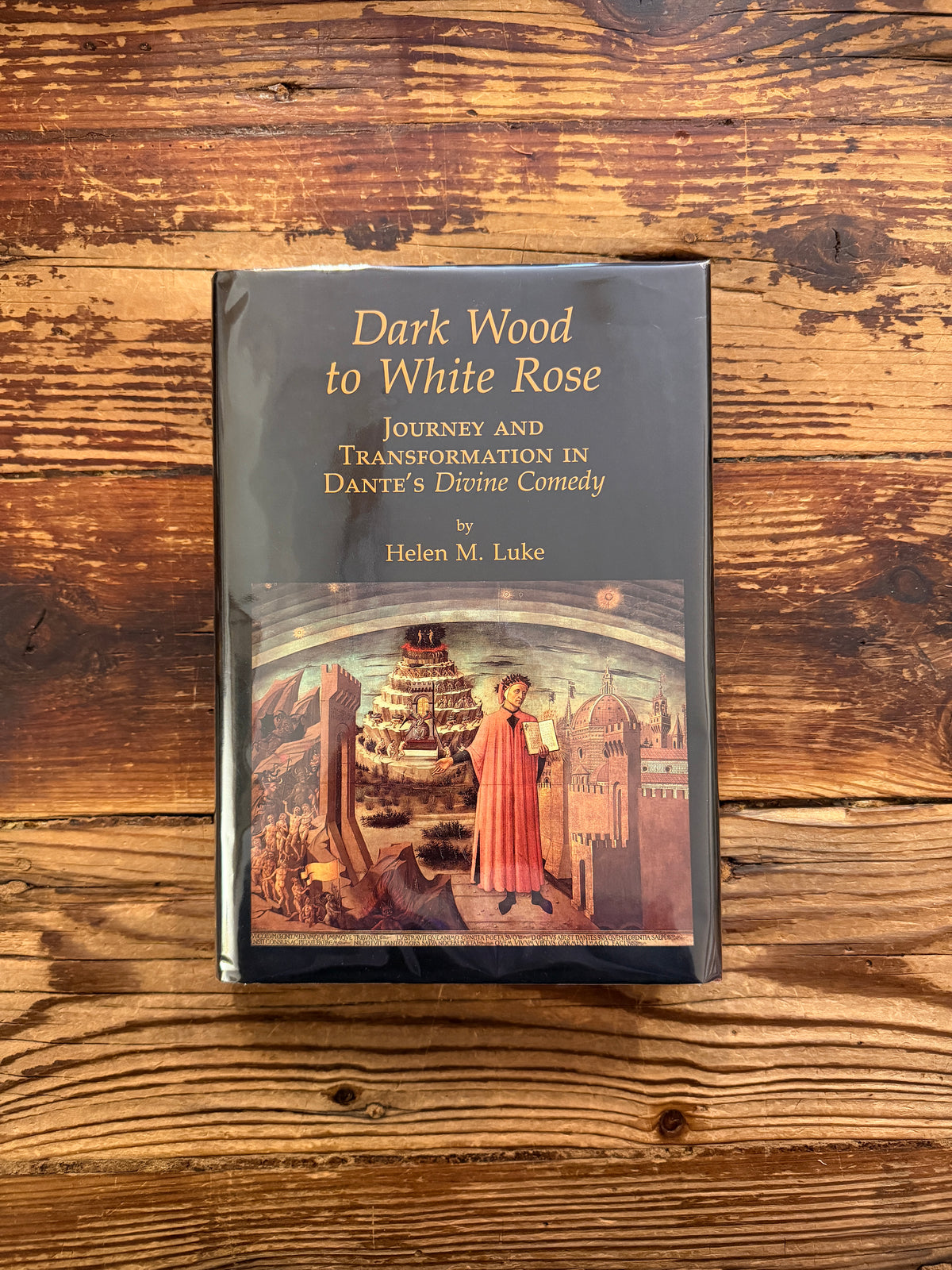 Front cover of a book with the title 'Dark Wood to White Rose, journey and transformation in Dante’s Divine Comedy' by Helen M. Luke on a wooden surface 