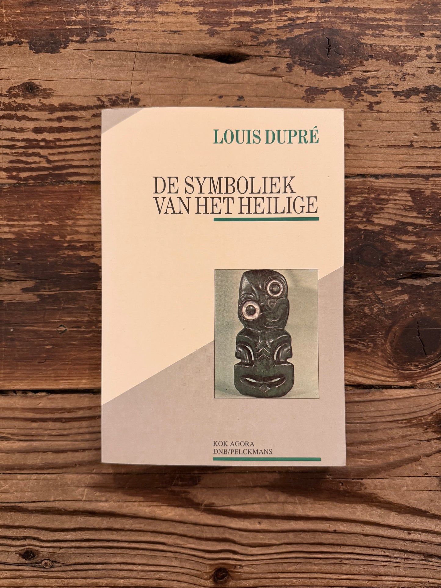 Voorkant van een boek met de titel 'de symboliek van het heilige' door Louis Dupré op een houten achtergrond 
