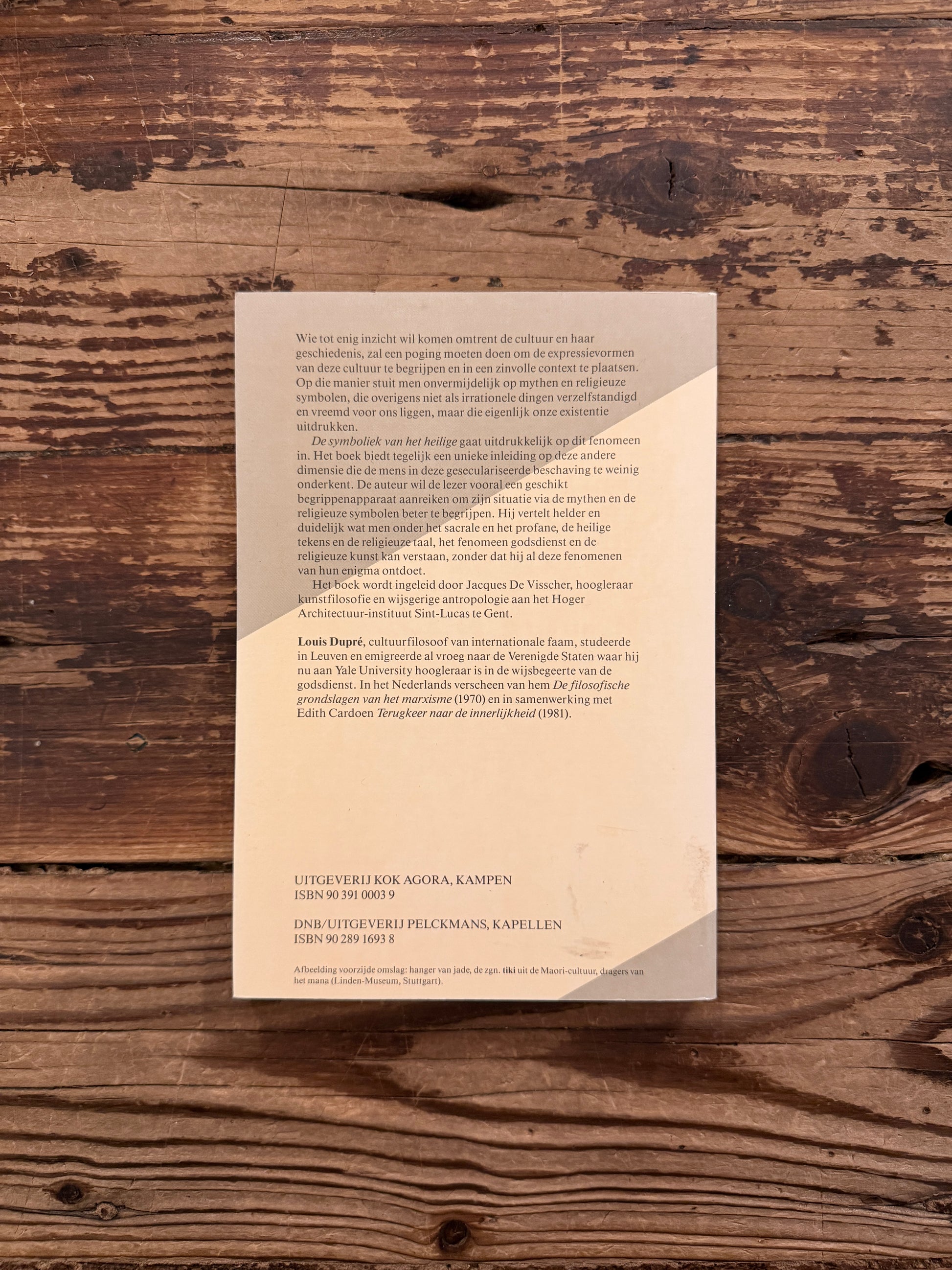 Achterkant van een boek met de titel 'de symboliek van het heilige' door Louis Dupré op een houten achtergrond 