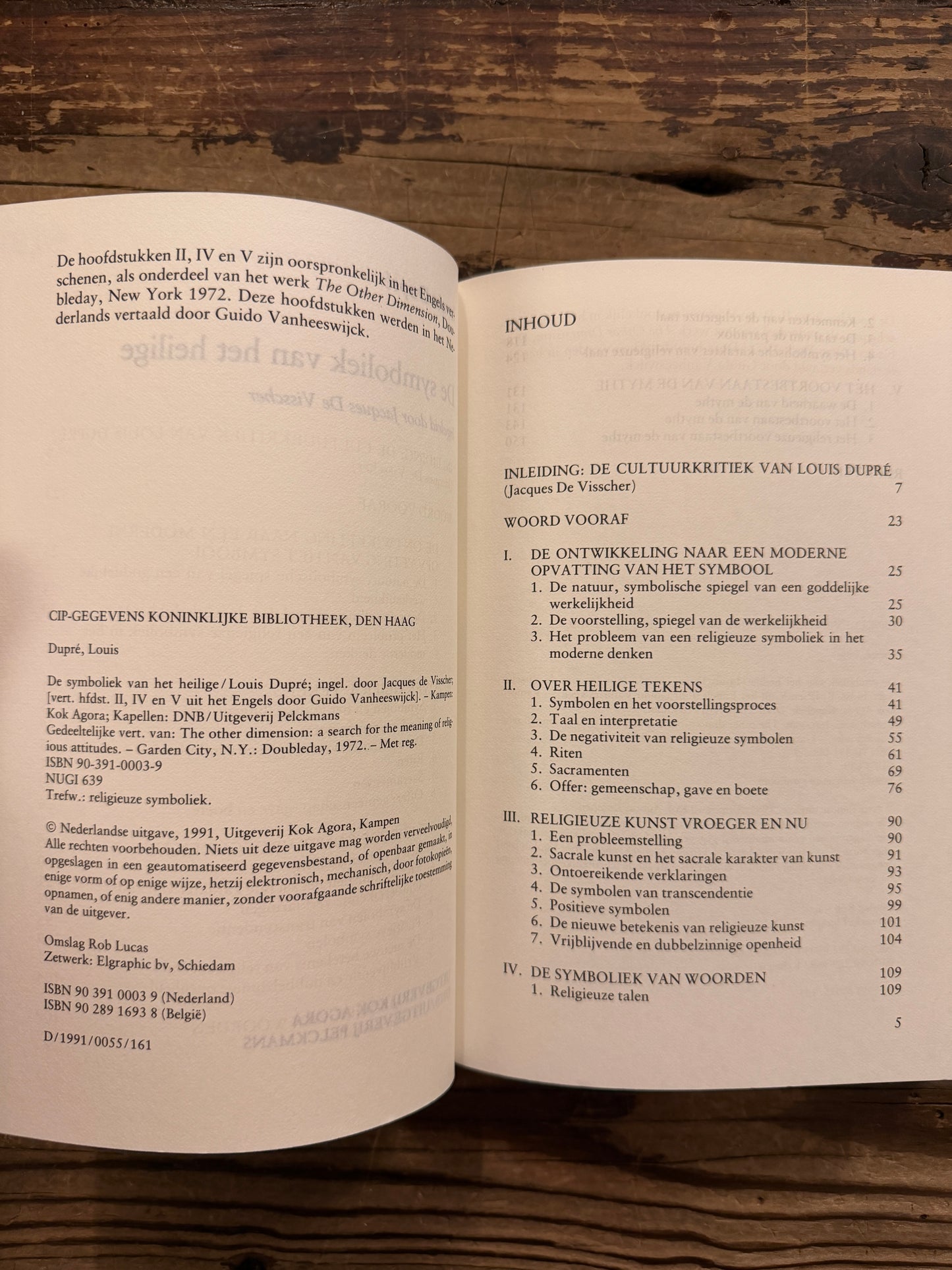 Open boek met de titel 'de symboliek van het heilige' door Louis Dupré op een houten achtergrond 