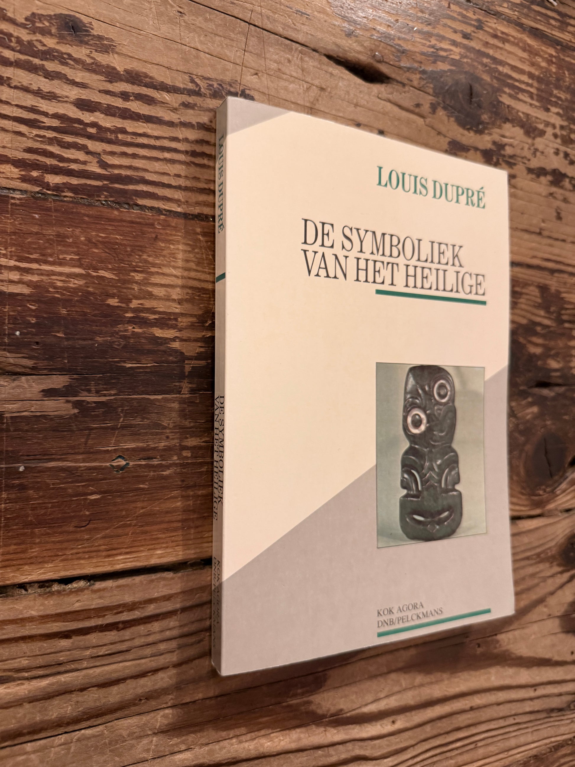 Voorkant en rug van een boek met de titel 'de symboliek van het heilige' door Louis Dupré op een houten achtergrond 