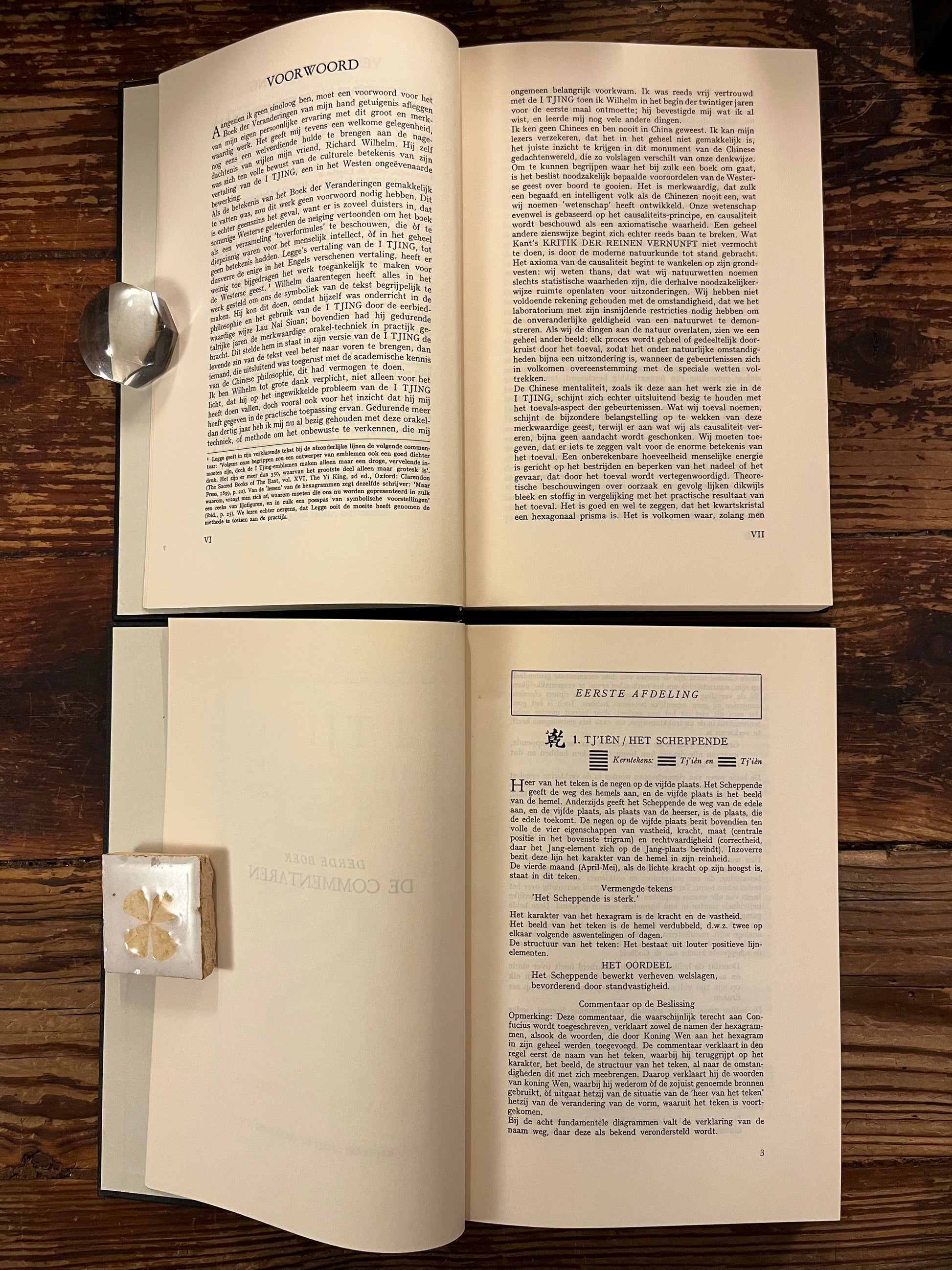 Twee open boeken met de titel 'I Tjing: Het Boek Der Veranderingen' op een houten achtergrond