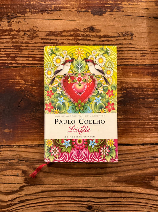 Voorkant van boek met de titel 'liefde' door Paulo Coelho op een houten achtergrond