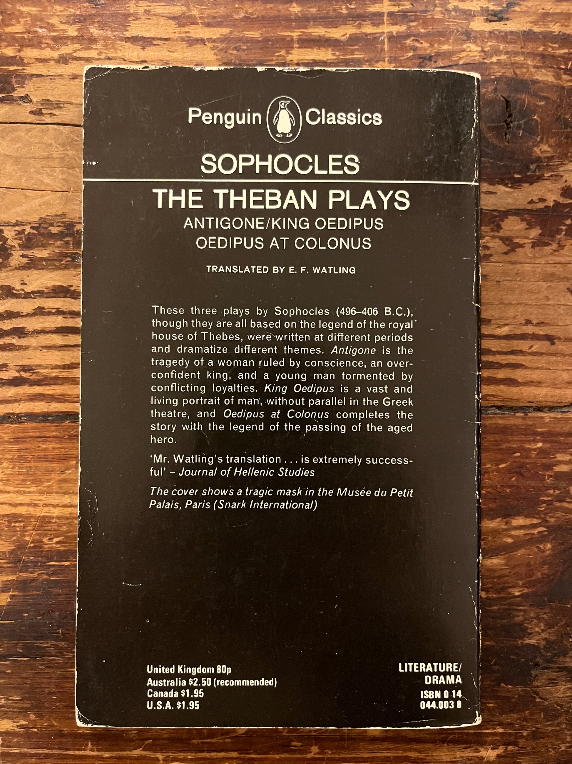 Back cover of book titled 'The Theban Plays' by Sophocles on a wooden surface