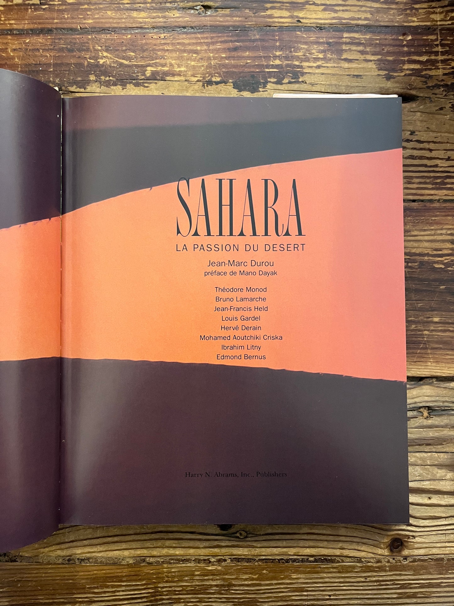 Book titled 'Sahara: The Forbidding Sands' by Jean-Marc Durou on a wooden surface