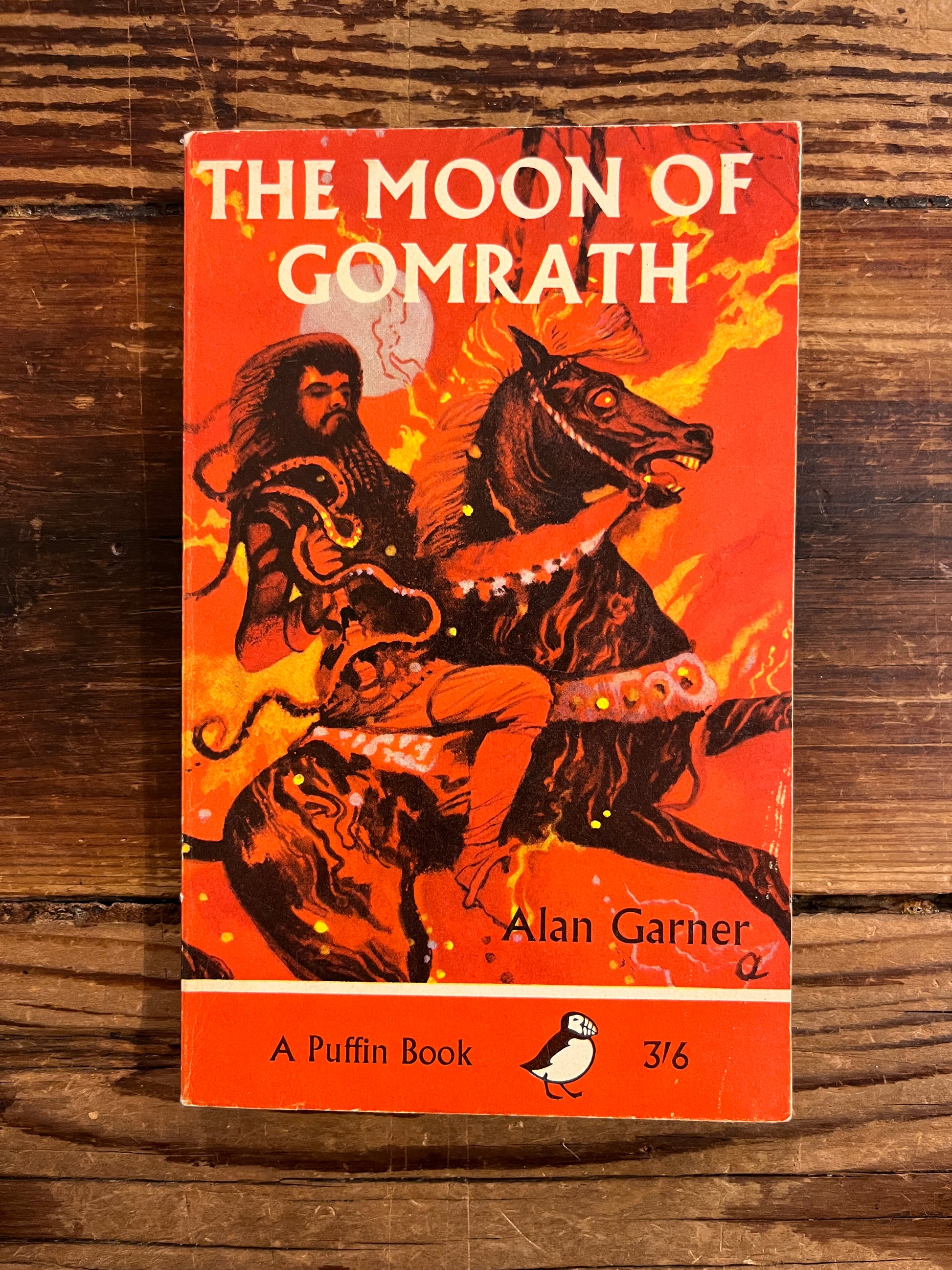 Book cover of 'The Moon of Gomrath' by Alan Garner on a wooden surface