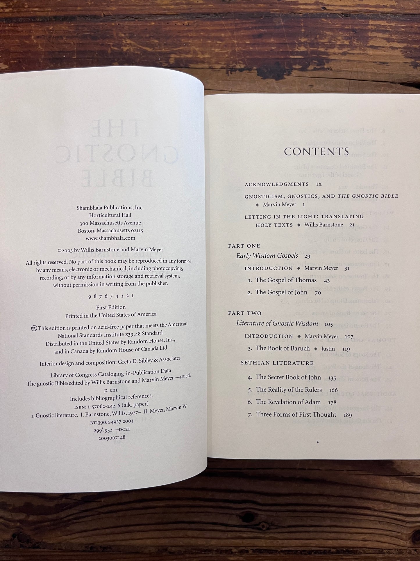 Open book titled 'he Gnostic Bible' edited by Willis Barnstone and Marvin Meyer, on a wooden surface