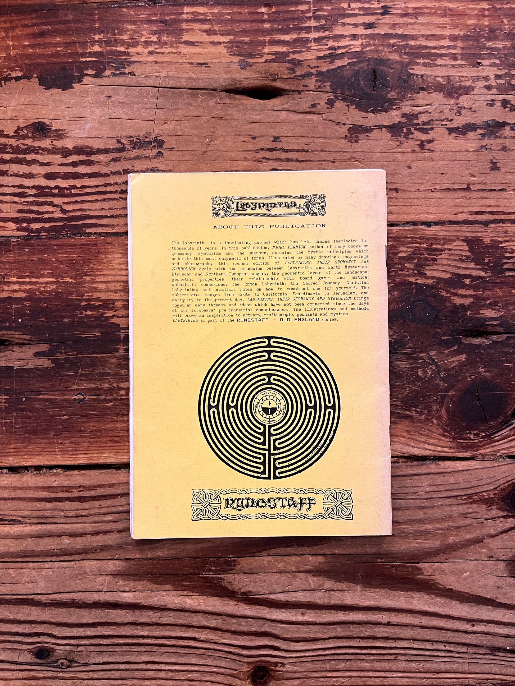 Back cover of booklet with the title 'Labyrinths, their geomancy and symbolism' by Nigel Pennick on a wooden surface 