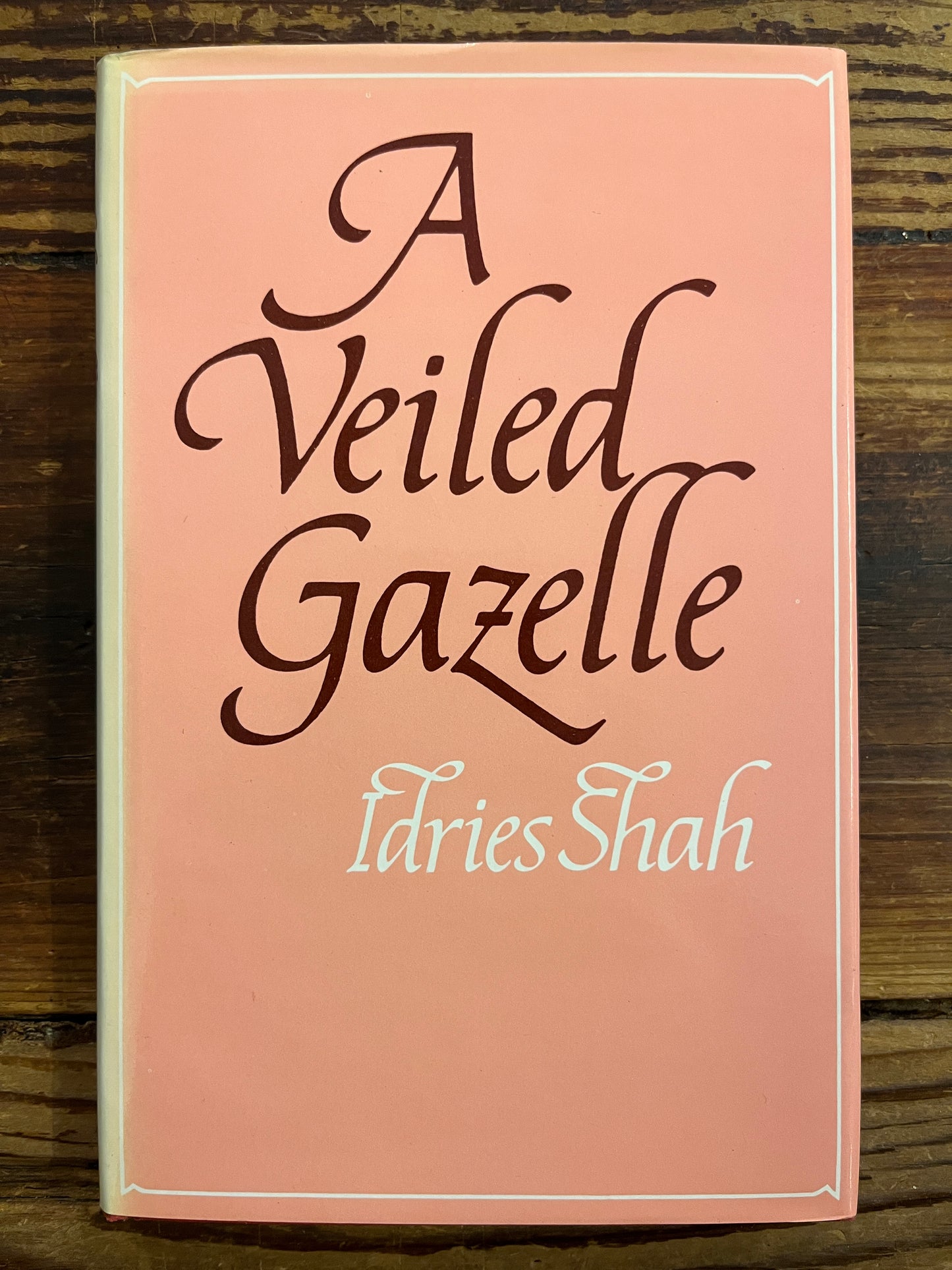 Book titled 'A Veiled Gazette' by Idries Shah on a wooden surface