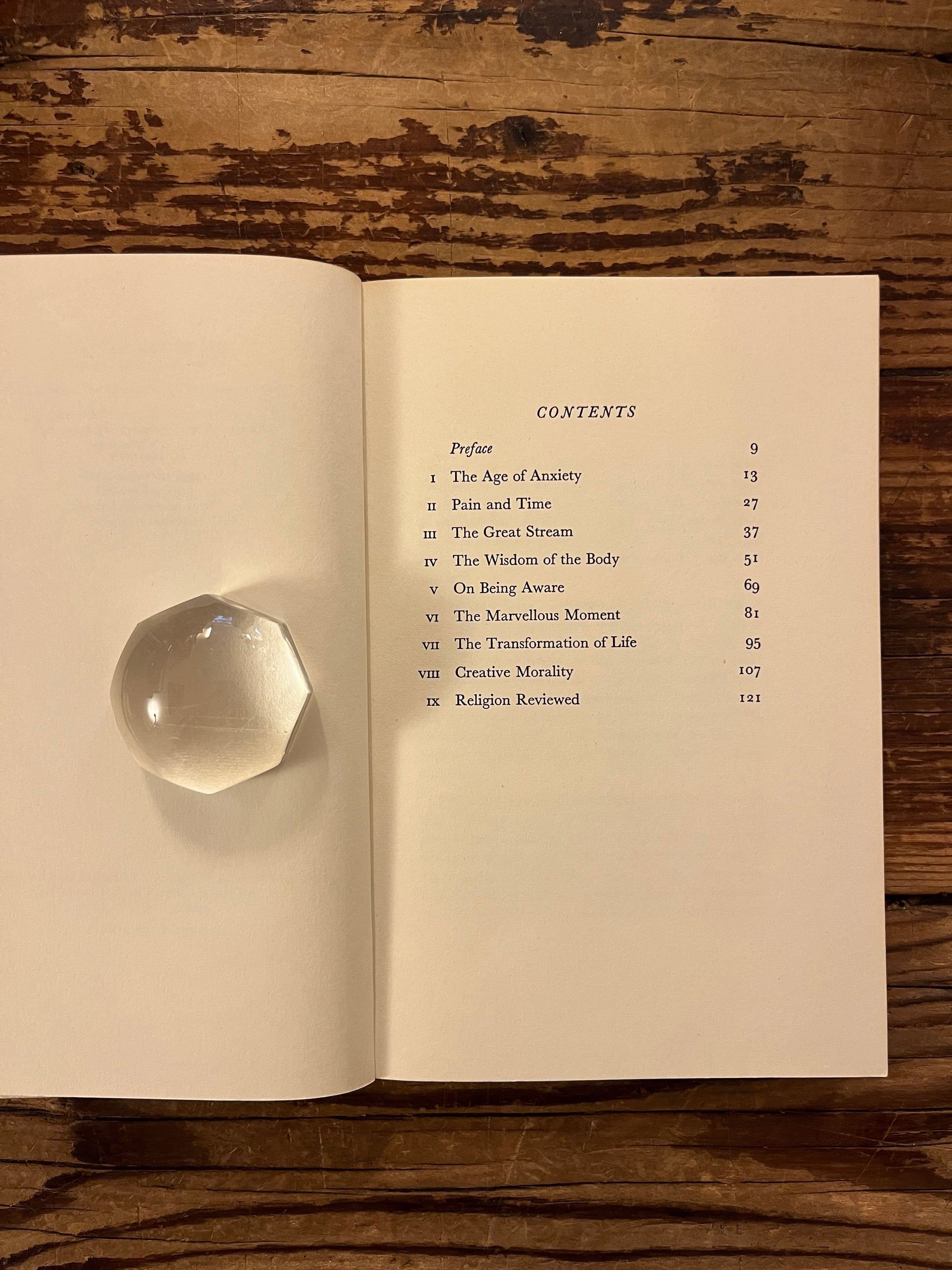 Open book with the title 'The Wisdom of Insecurity' by Alan W. Watts on a wooden surface