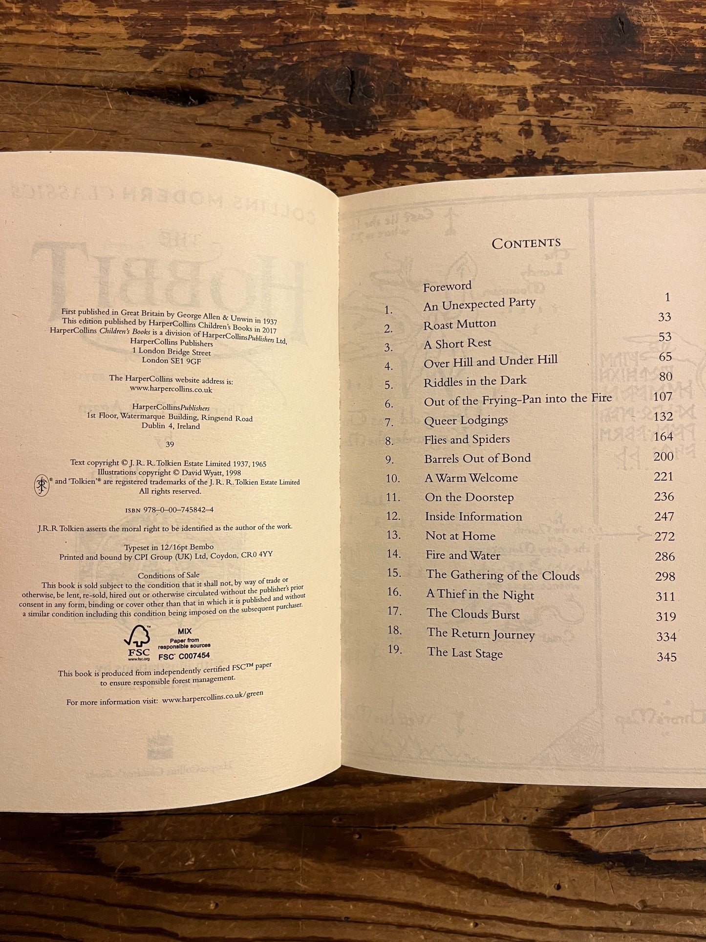 Open book showing the contents of a book titled 'The Hobbit' by J.R.R. Tolkien on a wooden surface