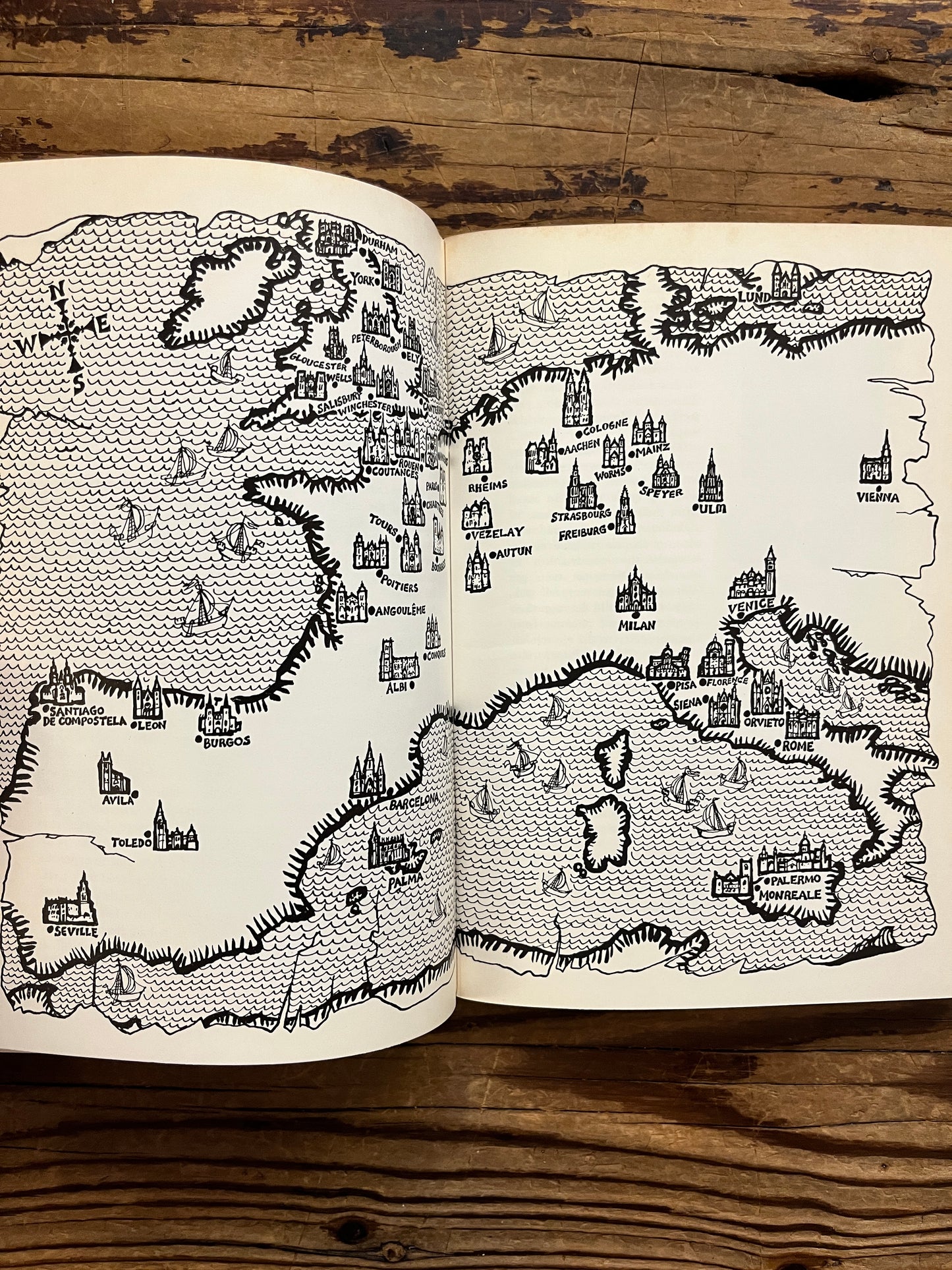 Open book titled 'Canterbury: the story of a cathedral' showing an ancient map of Europe and its cathedrals, lying on a wooden surface 