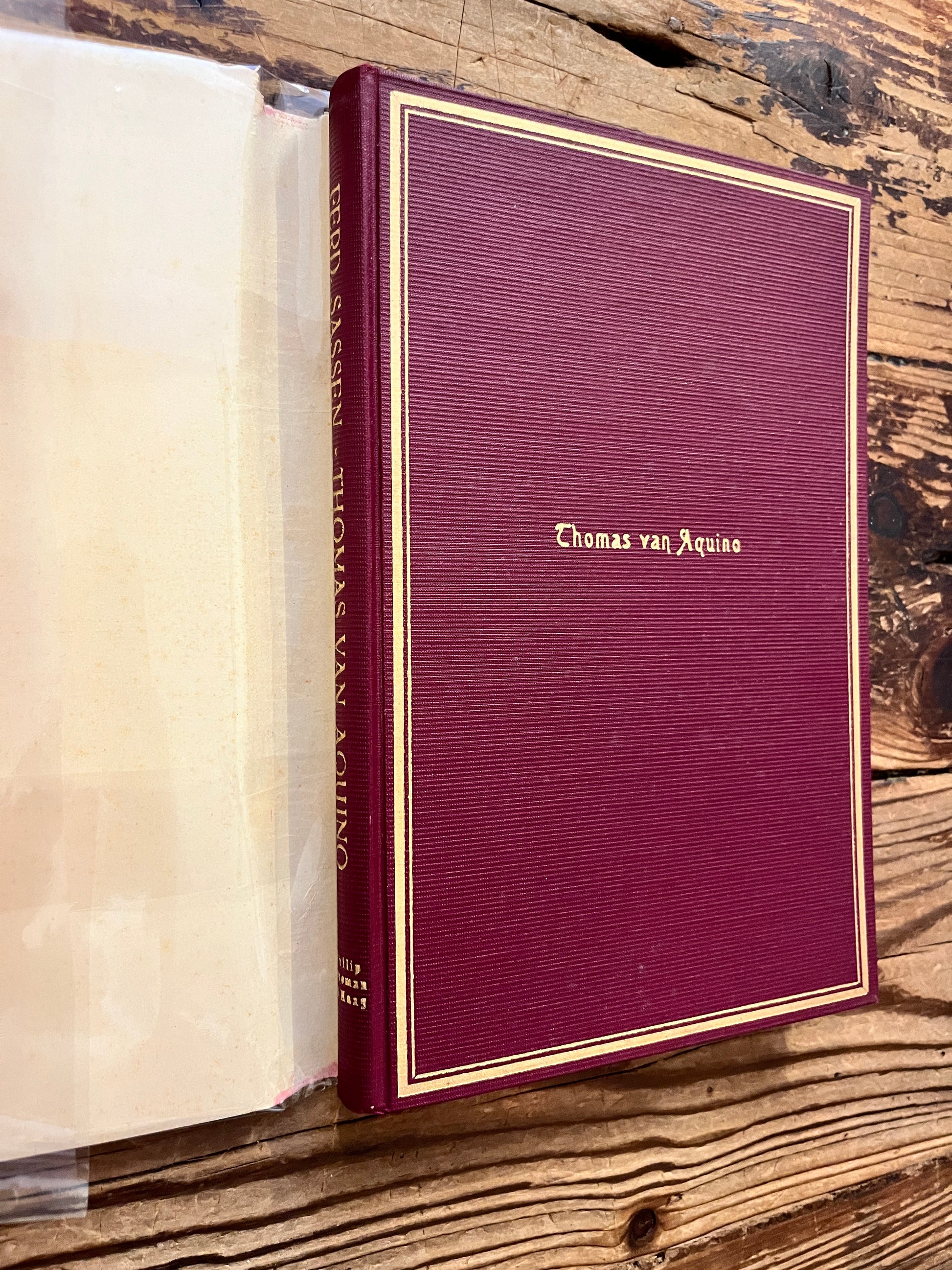 Voorkant zonder stof omslag van boek met de titel 'Thomas van Aquino' door Dr. Ferd. Sassen op een houten achtergrond  