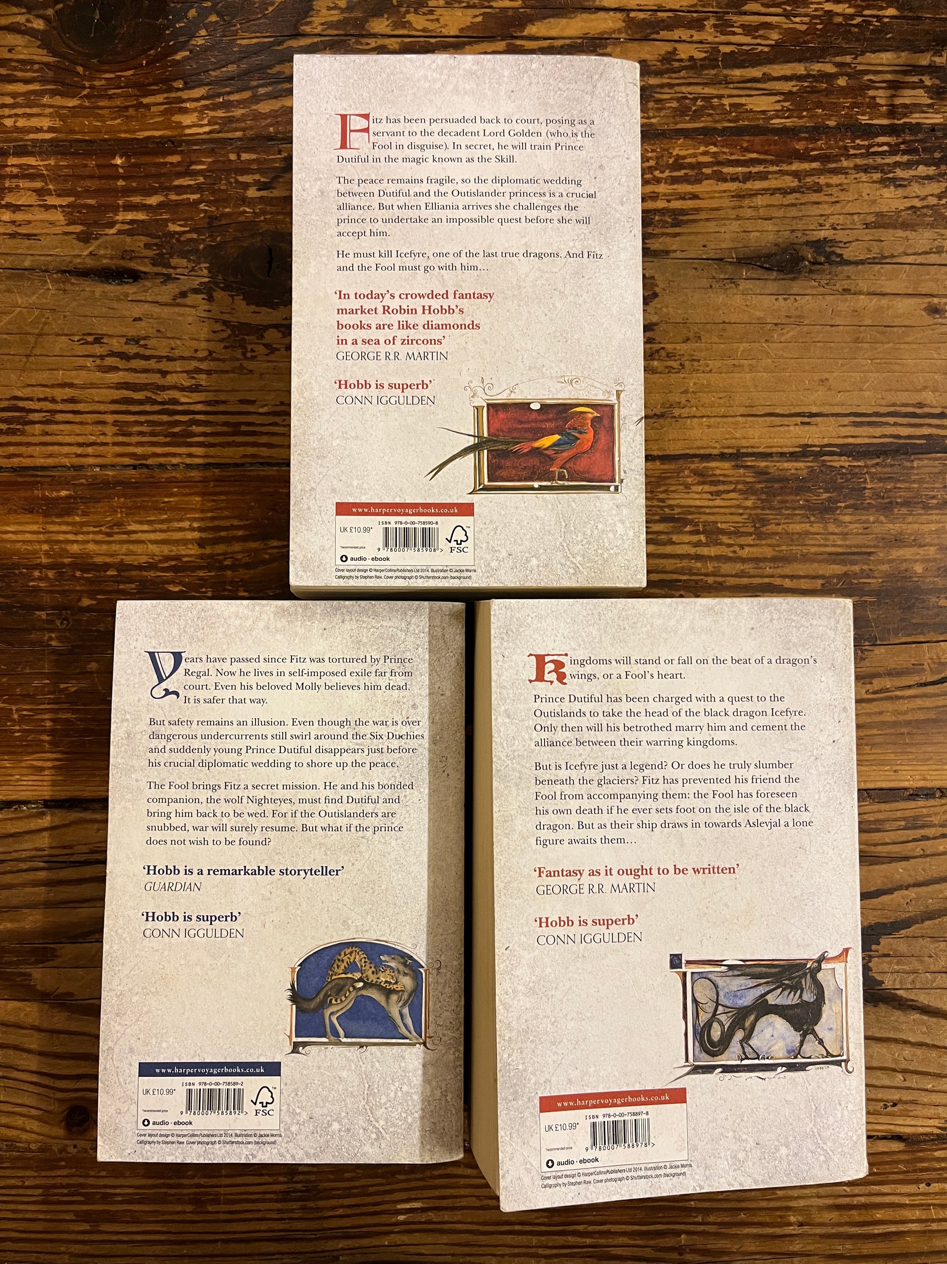 Back cover of the three books of Robin Hobb's 'Tawny Man's trilogy' on a wooden surface