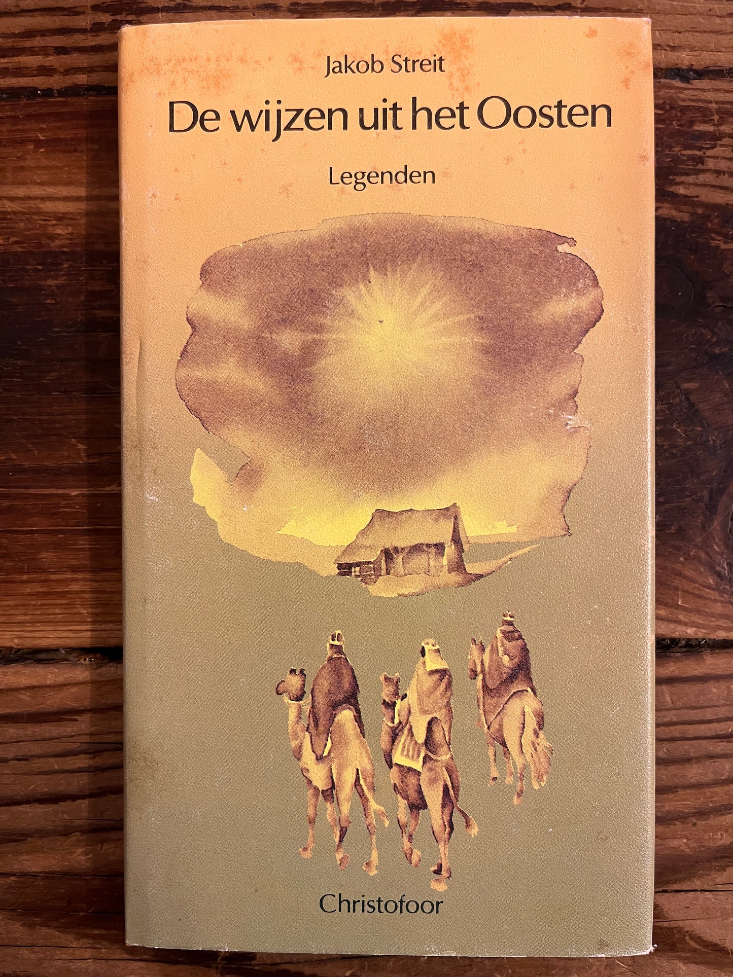 Voorkant met stof omslag van boek met de titel 'De wijzen uit het Oosten' door Jakob Streit op een houten achtergrond 