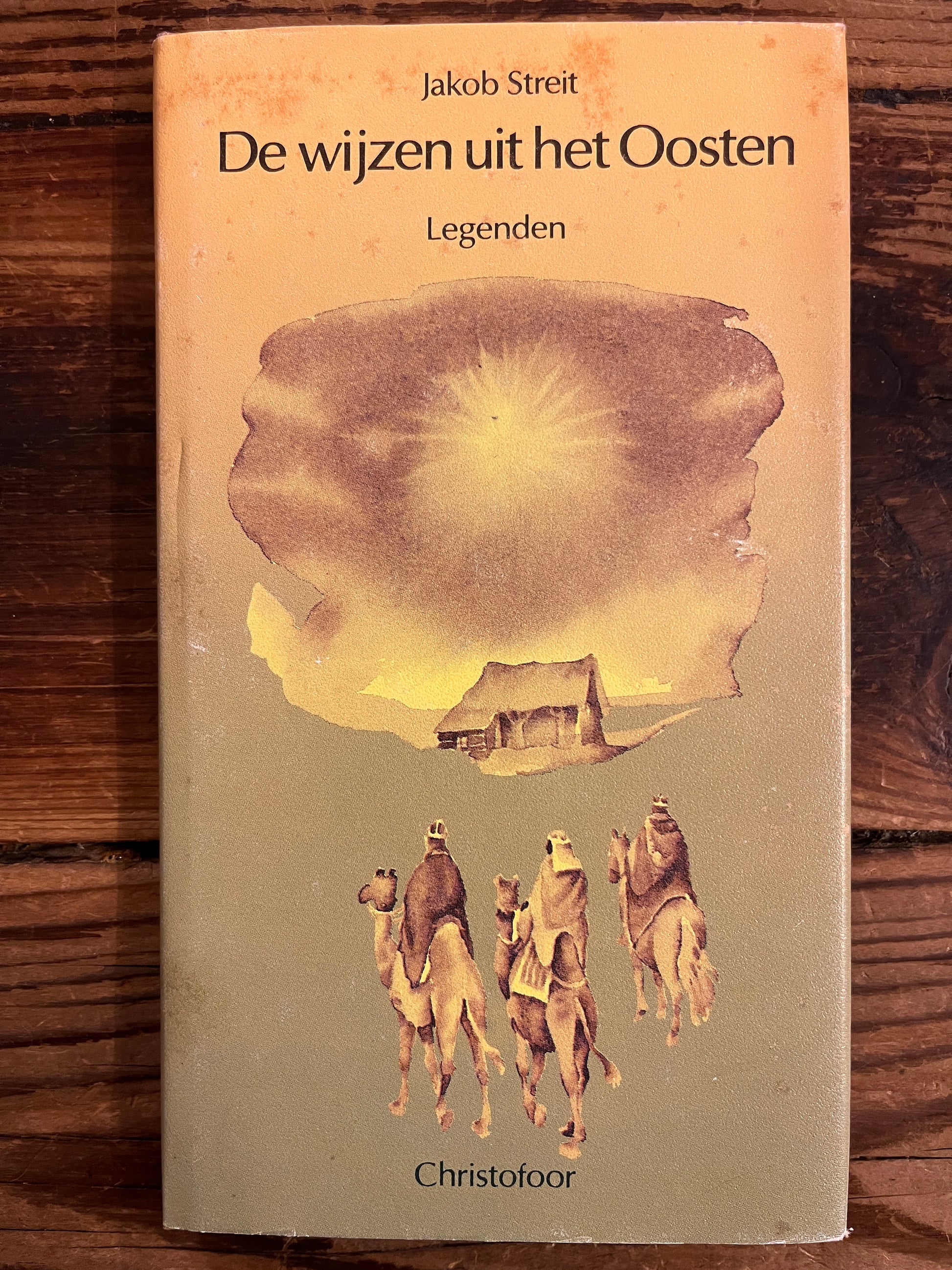Voorkant met stof omslag van boek met de titel 'De wijzen uit het Oosten' door Jakob Streit op een houten achtergrond 