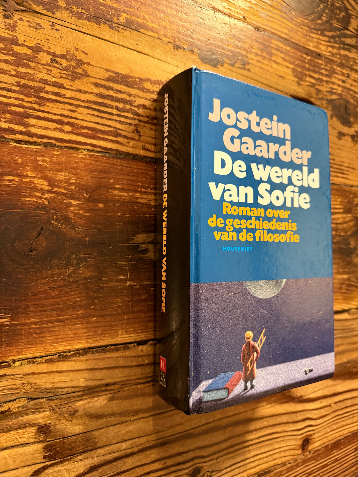 Voorkant en rug van boek met de titel 'De wereld van Sofie' door Jostein Gaarder, op een houten achtergrond