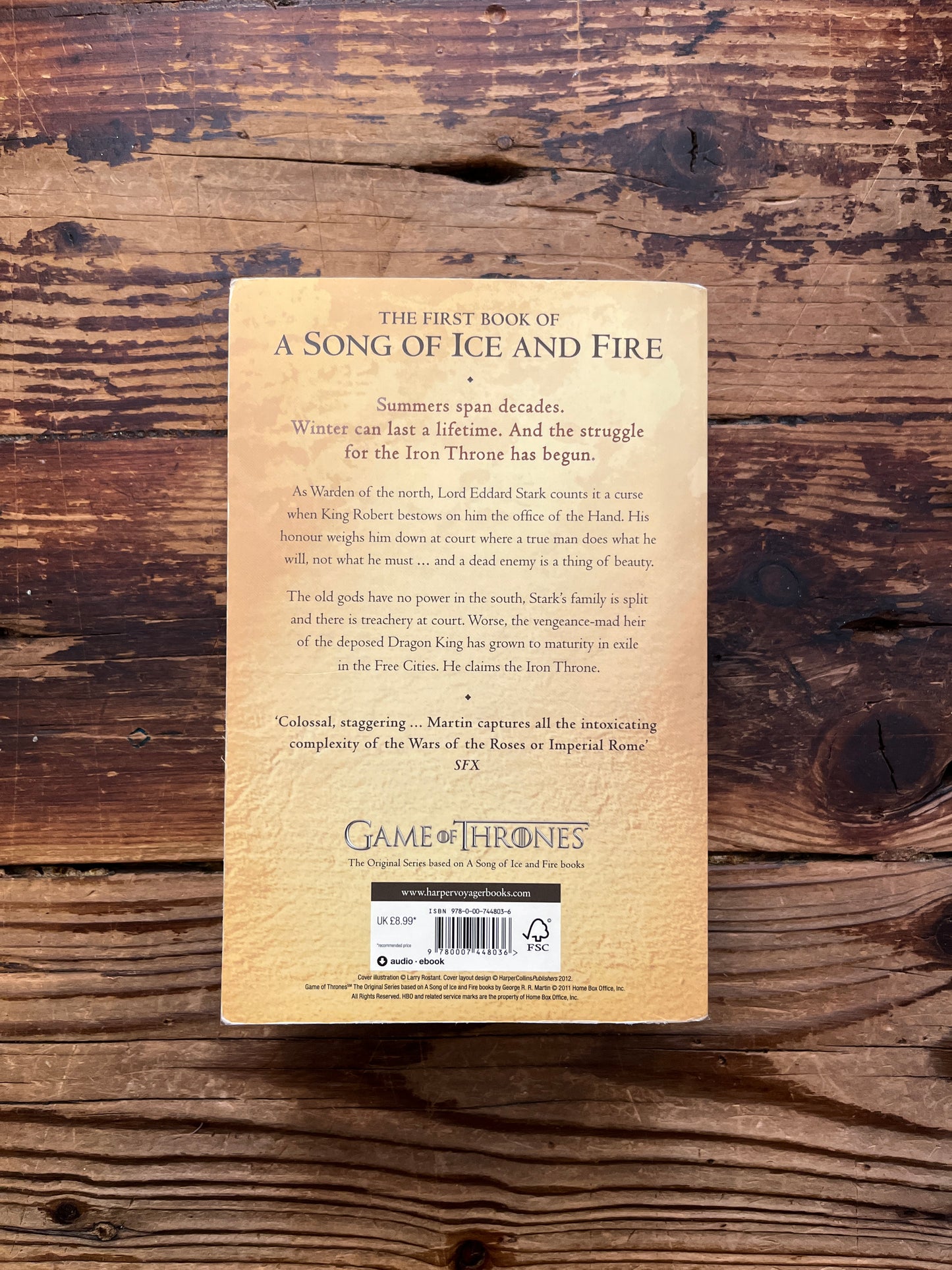 Back cover of book titled 'A Game of Thrones' by George R.R. Martin on a wooden surface