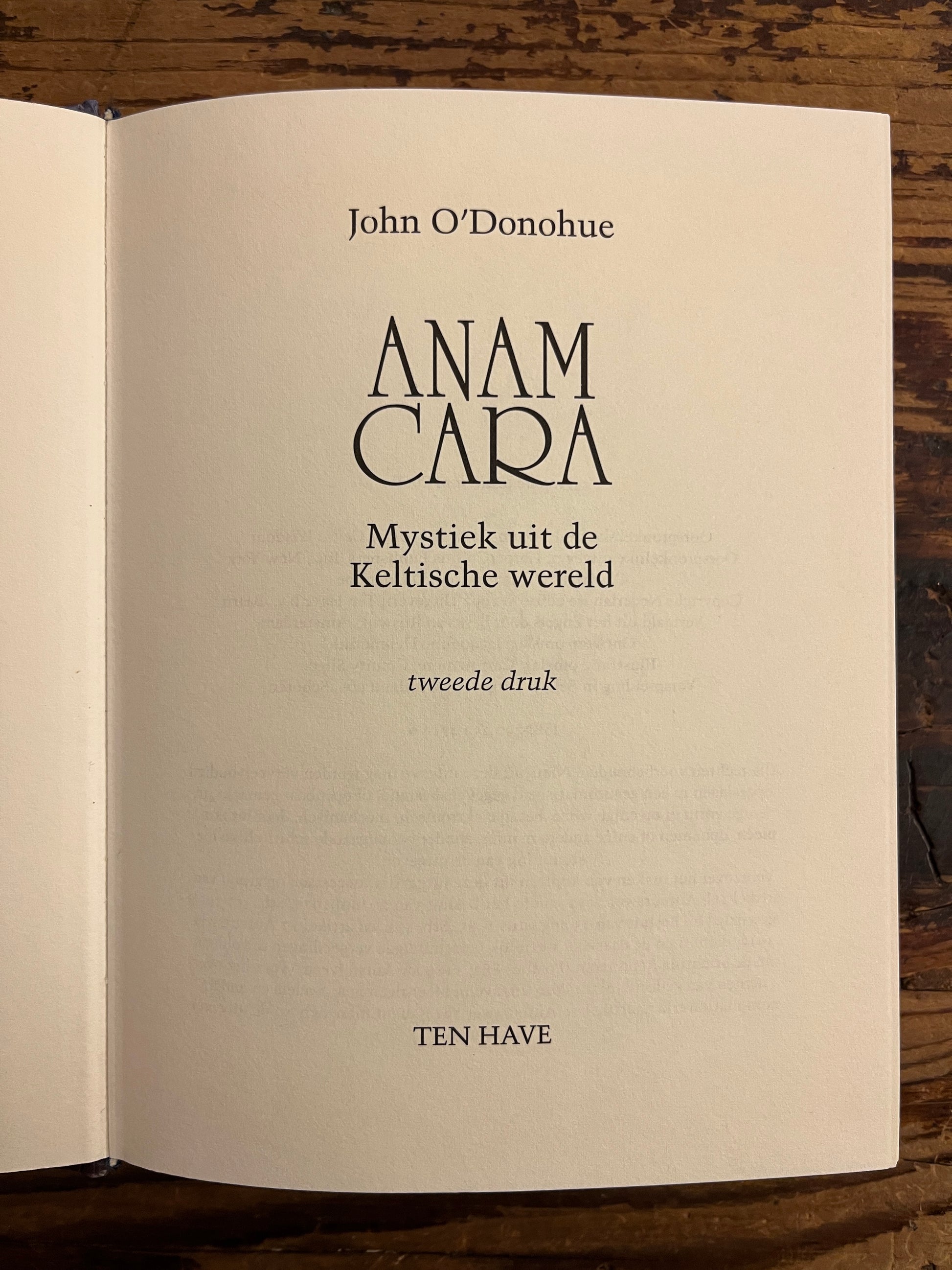 Open boek met de titel 'Anam Cara: Mystiek uit de Keltische wereld, tweede druk' door John O'Donohue op een houten achtergrond 