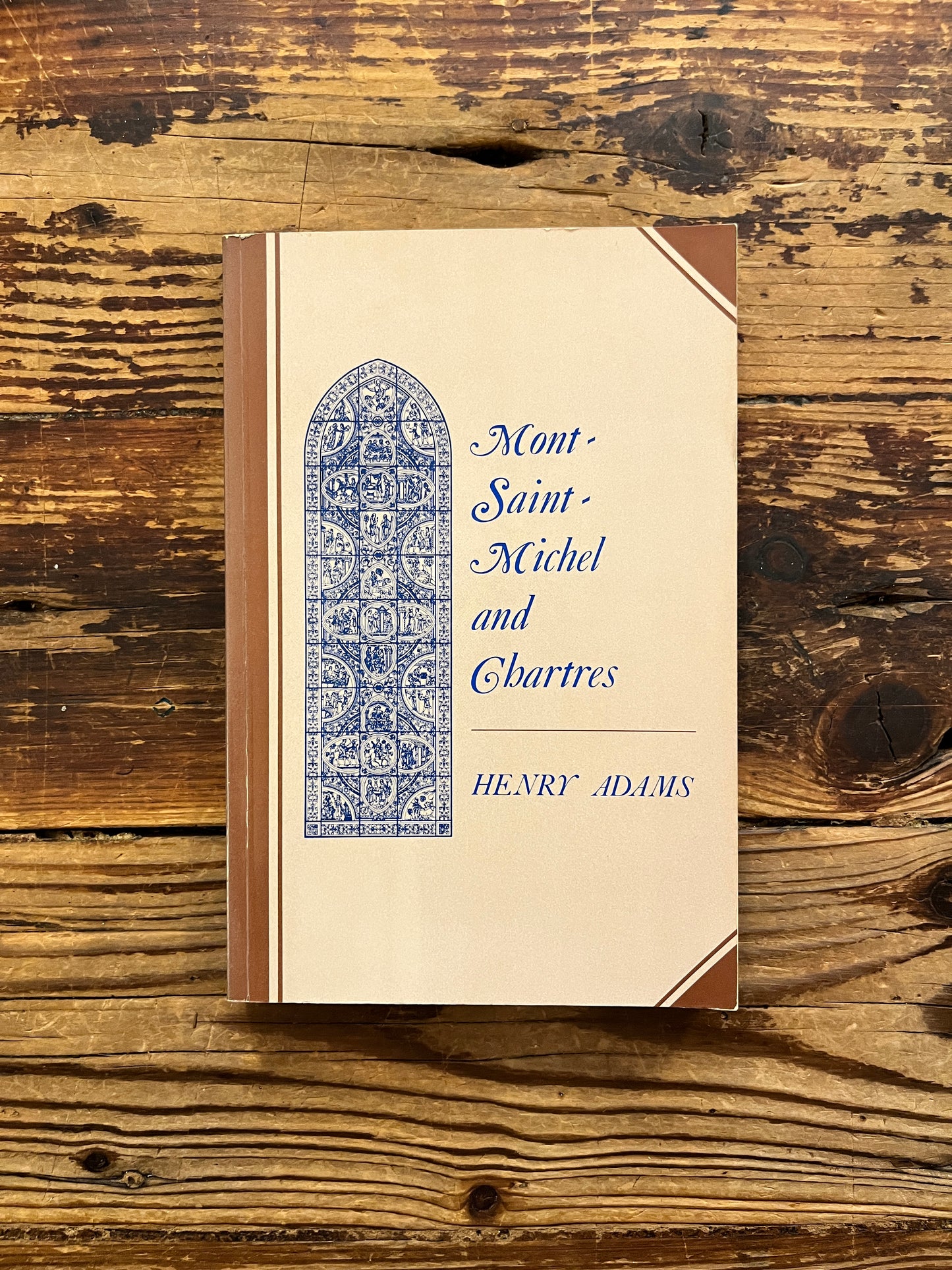 Front cover of a book titled 'Mont Saint-Michel and Chartres' by Henry Adams on a wooden surface