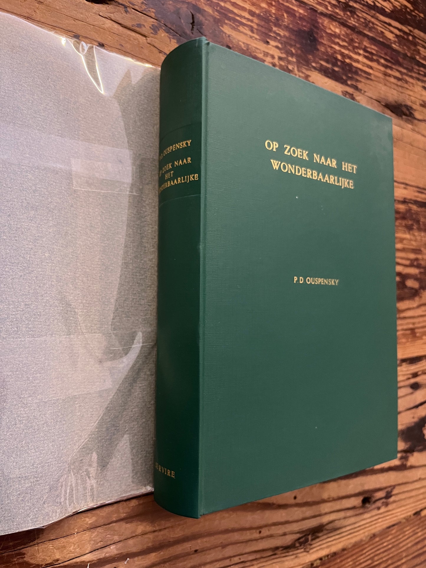 Rug en voorkant van boek zonder stof omslag met de titel 'op zoek naar het wonderbaarlijke, fragmenten van een onbekende leer' door P. D.  Ouspensky op een houten achter grond 