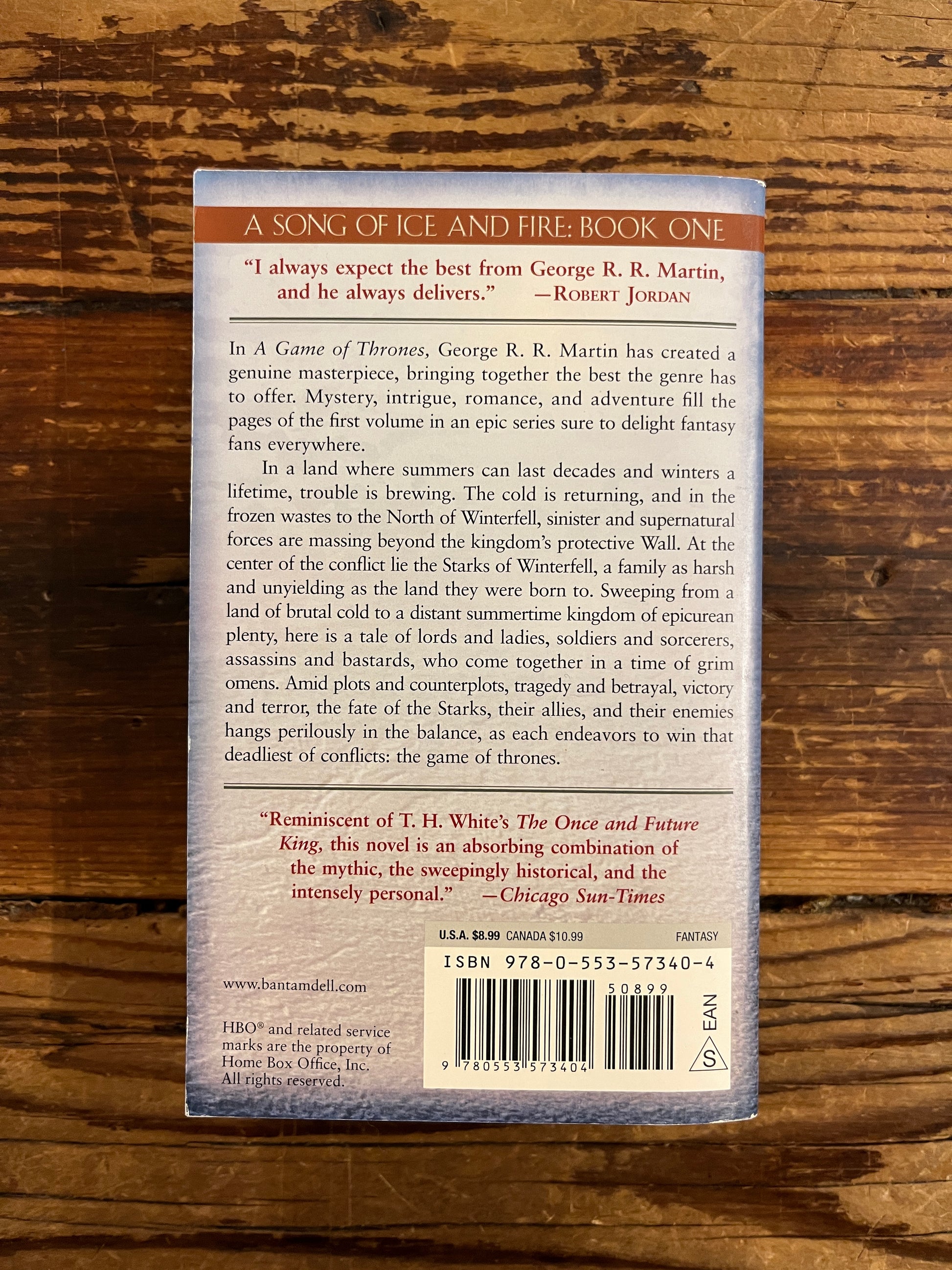 Back cover of a book titled ' a game of thrones' by George R. R. Martin on a wooden surface