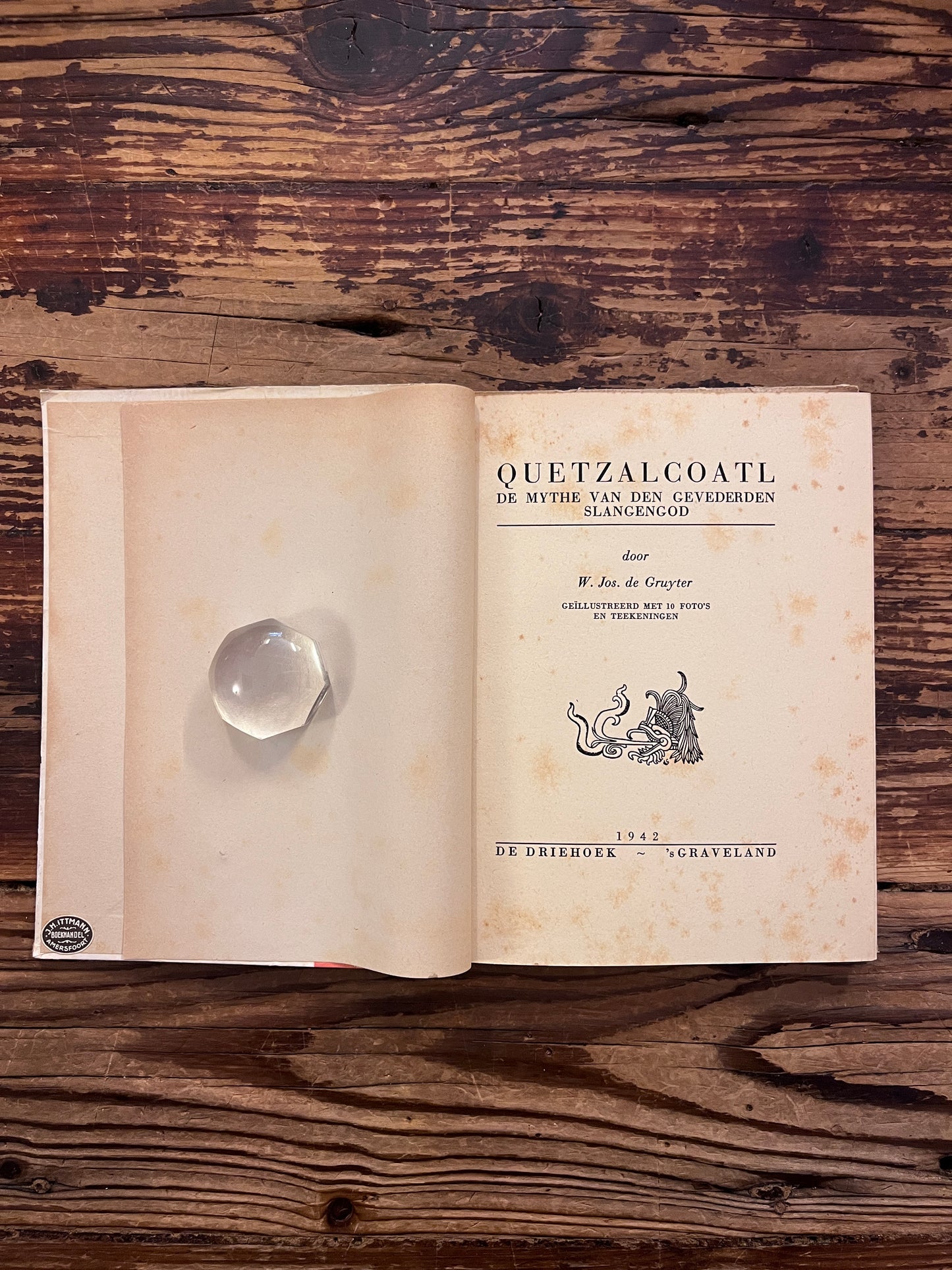 Open boek met de titel 'Quetzalcoatl: De mythe van den gevederden slangengod' door Jos de Gruyter op een houten achtergrond 