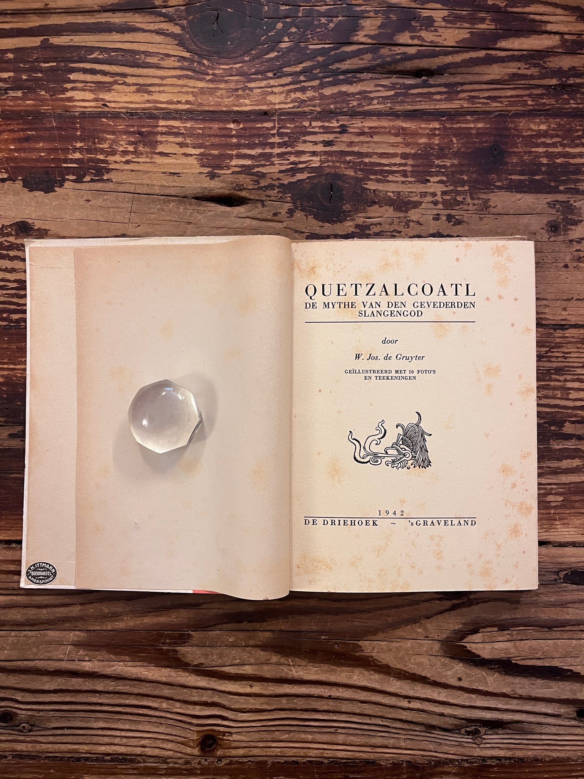 Open boek met de titel 'Quetzalcoatl: De mythe van den gevederden slangengod' door Jos de Gruyter op een houten achtergrond 