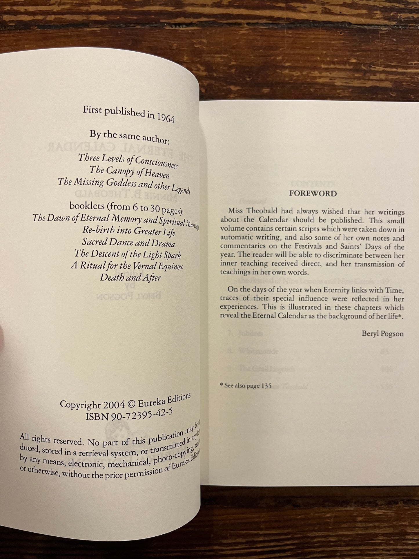 Open book titled 'The Eternal Calendar' by Minnie Theobald with a simple white design on the cover.