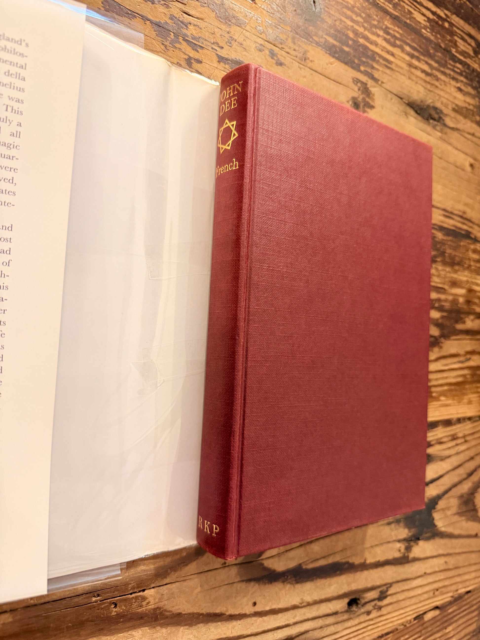 Front cover and spine without dust jacket of a book titled 'John Dee: The World of an Elizabethan Magus' by Peter J. French on a wooden surface