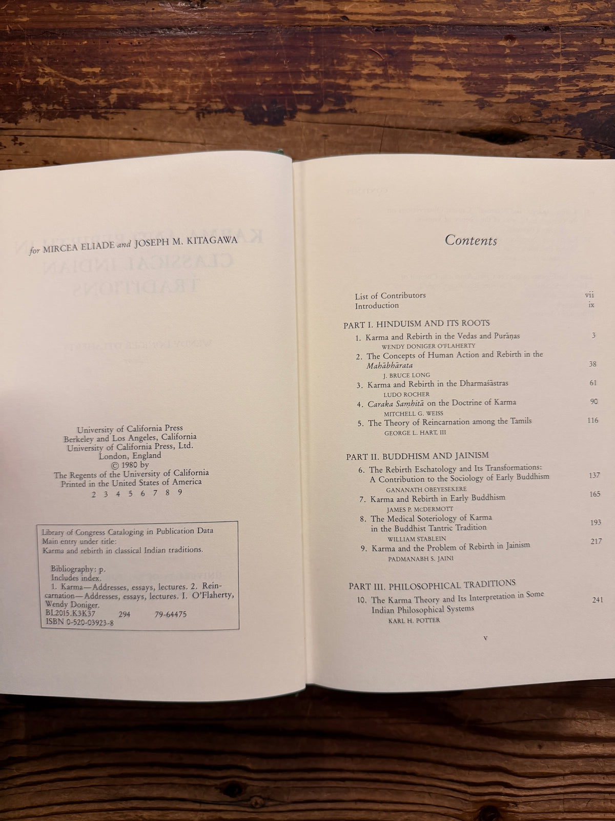 Open book titled 'Karma and Rebirth in Classical Indian Traditions' edited by Wendy Doniger O'Flaherty, on a wooden surface