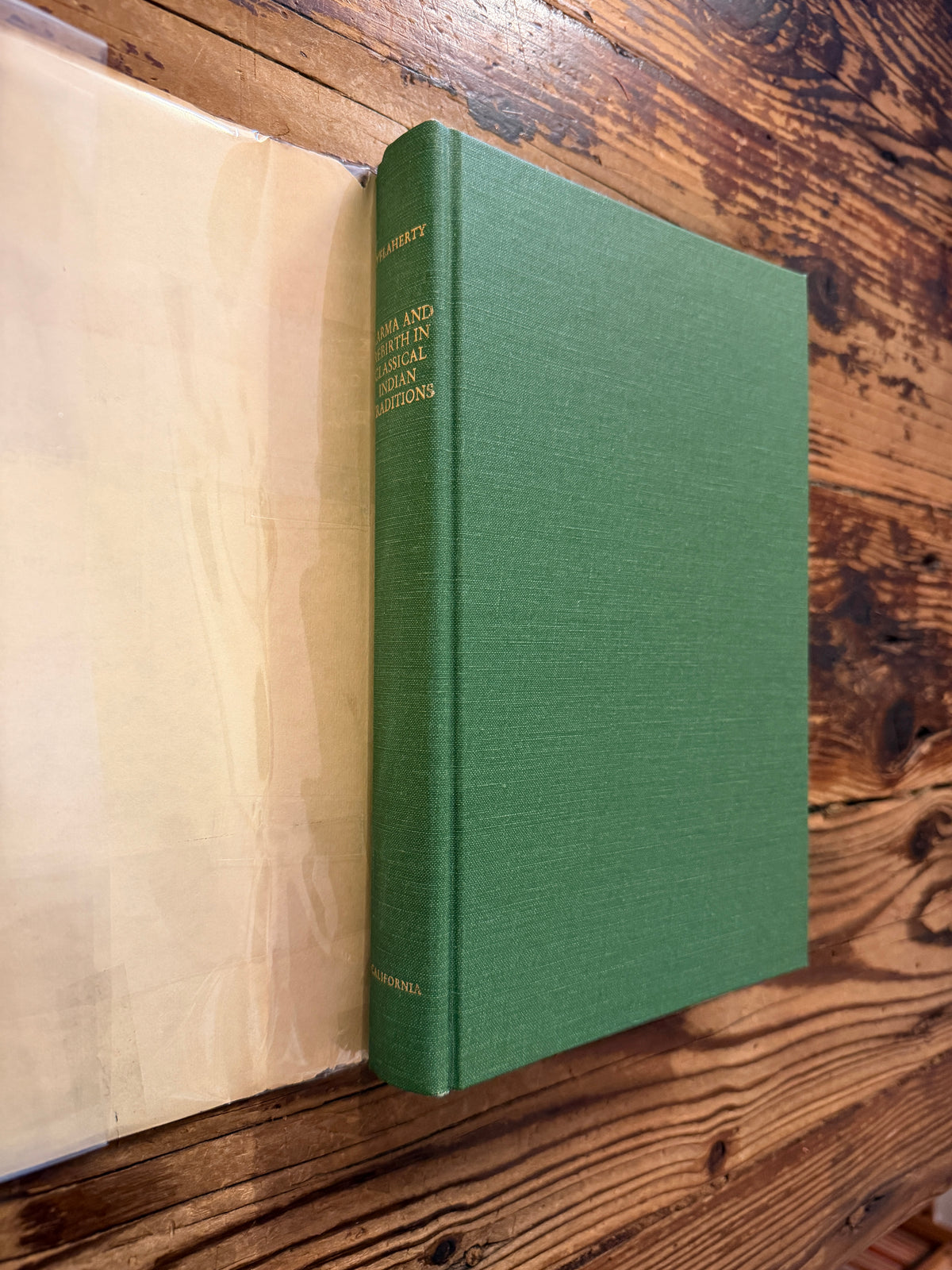 Front cover and spine without the dust jacket of a book titled 'Karma and Rebirth in Classical Indian Traditions' edited by Wendy Doniger O'Flaherty, on a wooden surface