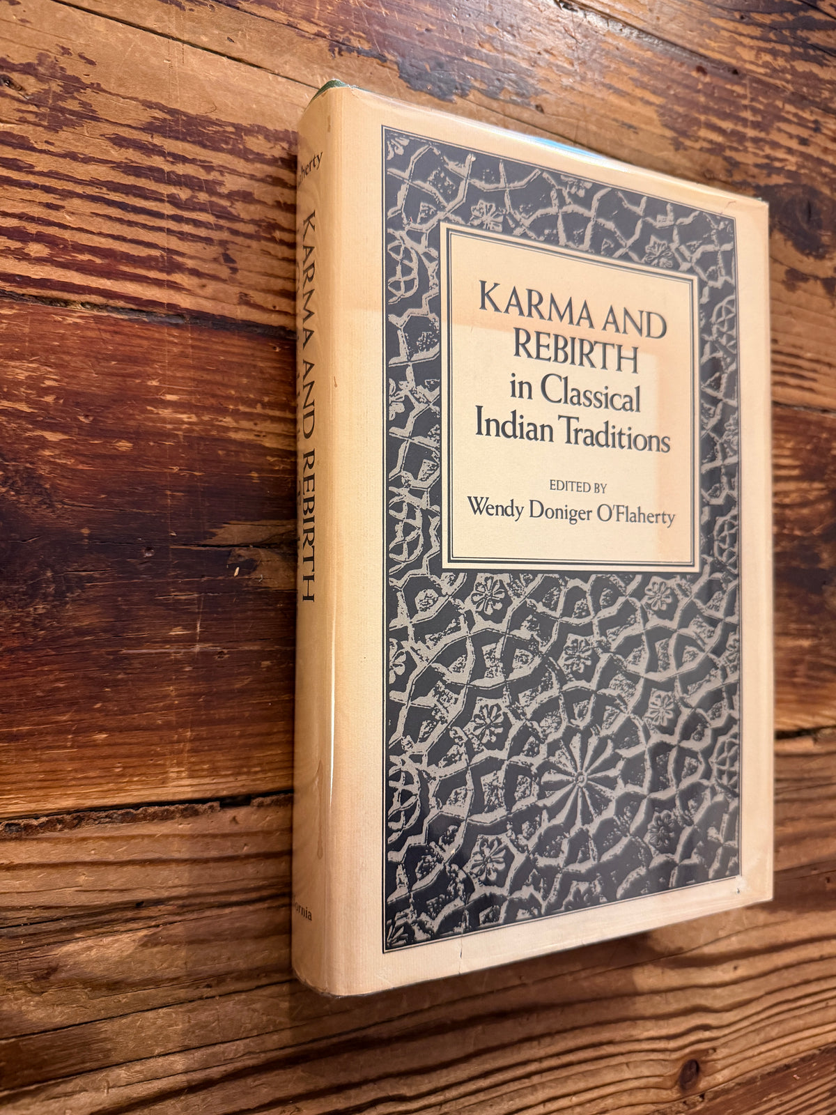 Front cover and spine of a book titled 'Karma and Rebirth in Classical Indian Traditions' edited by Wendy Doniger O'Flaherty, on a wooden surface