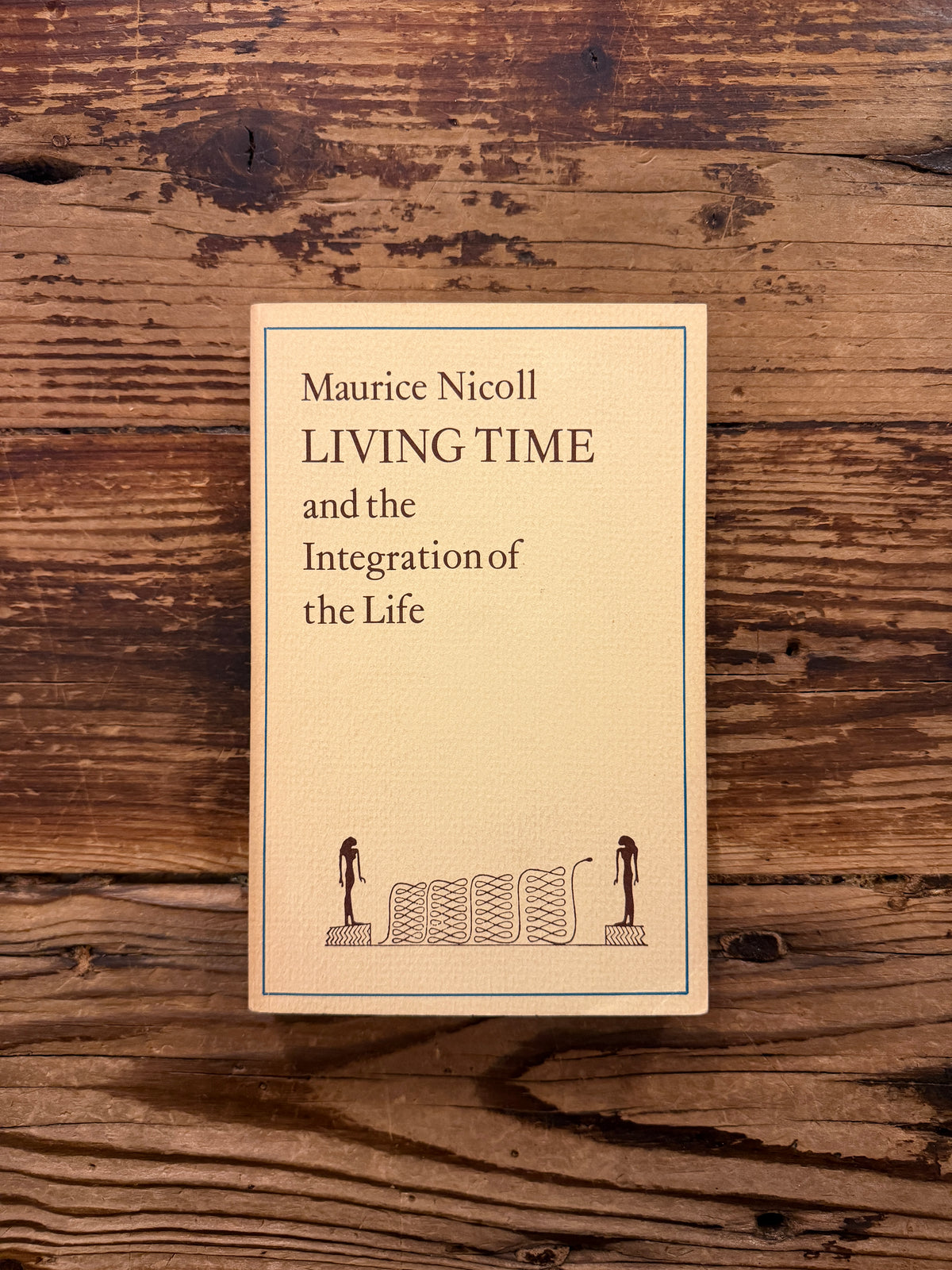 Front cover of a book with the title 'Living Time and the Integration of the Life' by Maurice Nicoll, a 1976 Watkins Edition lying on a wooden surface 