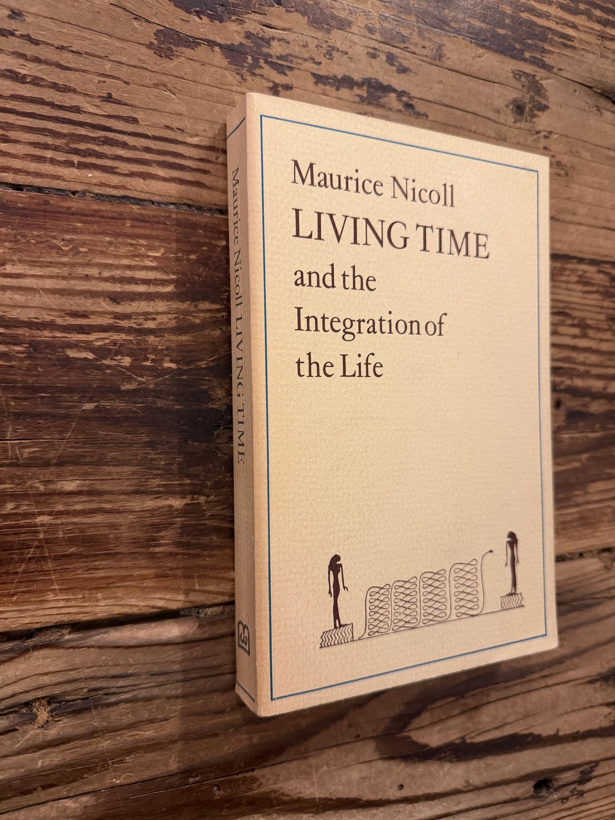 Front cover  and spine of a book with the title 'Living Time and the Integration of the Life' by Maurice Nicoll, a 1976 Watkins Edition lying on a wooden surface 