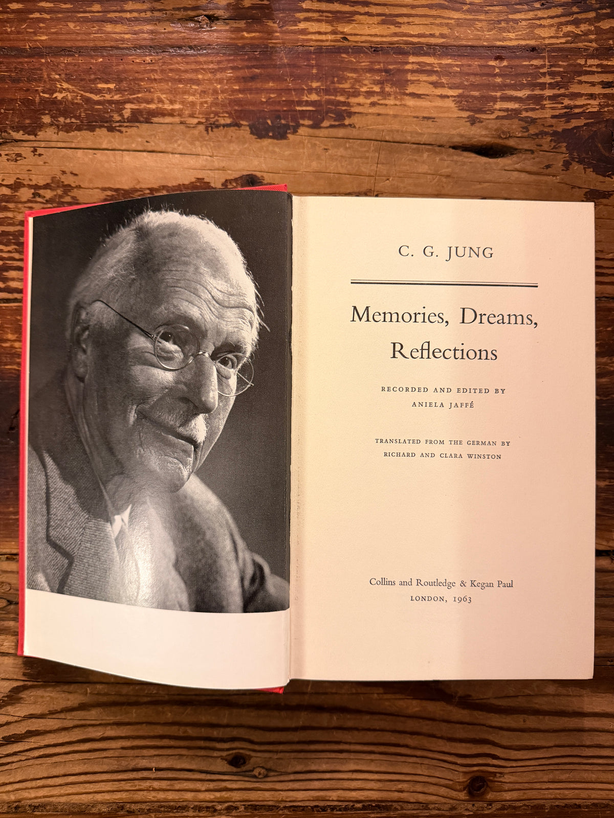 Open book with the titled 'Memories, Dreams, Reflections' by C.G. Jung, 1st English Edition 1963, on a wooden surface 
