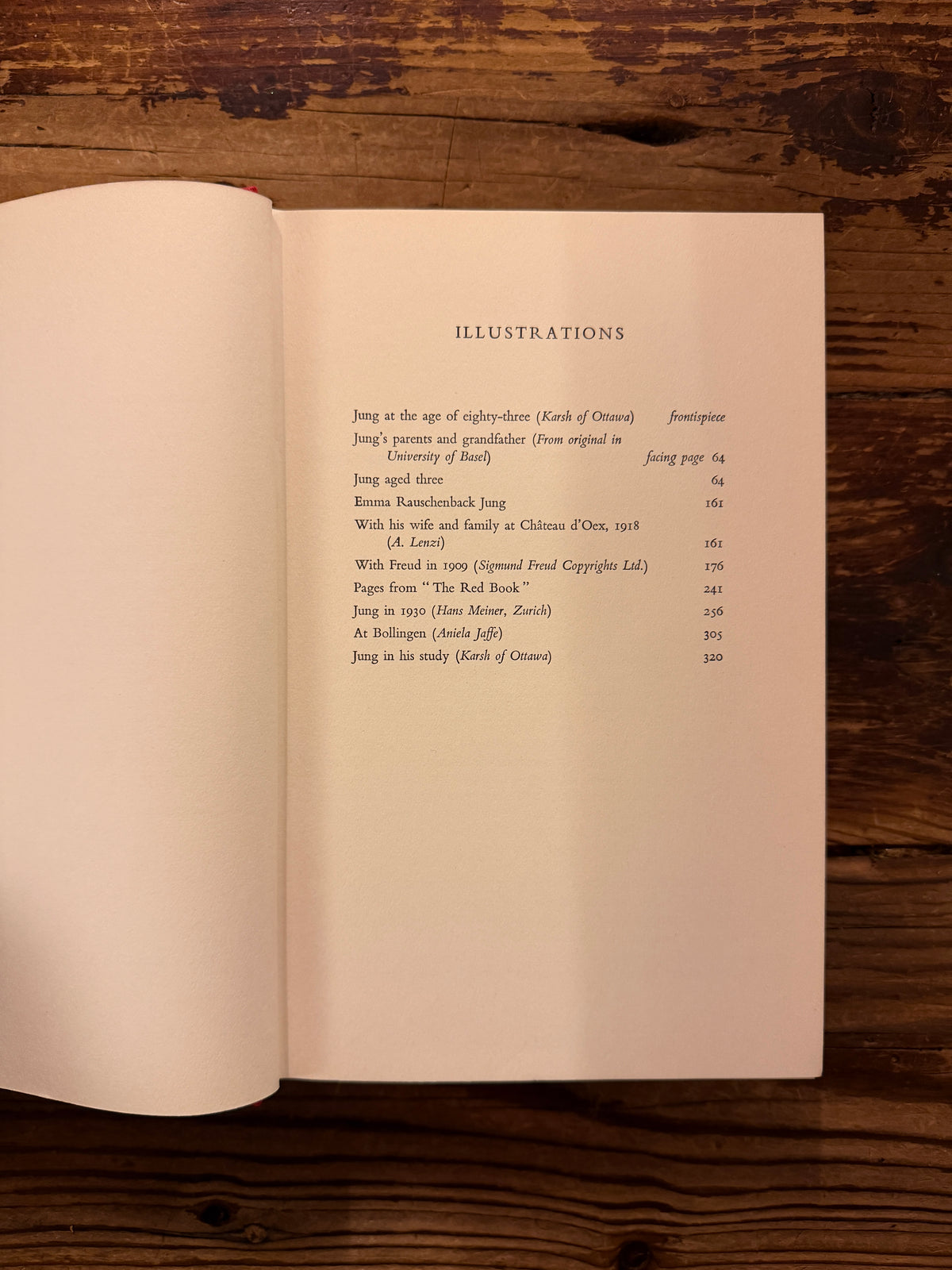 Open book with the titled 'Memories, Dreams, Reflections' by C.G. Jung, 1st English Edition 1963, on a wooden surface 