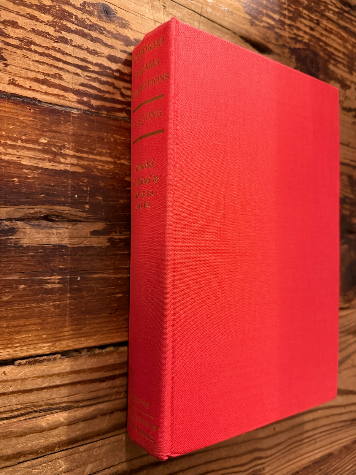 Spine and front cover book with the titled 'Memories, Dreams, Reflections' by C.G. Jung, 1st English Edition 1963, on a wooden surface 