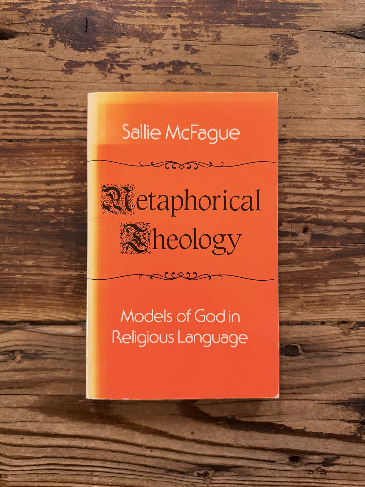 Front cover of a book with the title 'Metaphorical Theology, Models of God in Religious Language' by Sallie McFague, exposed on a wooden surface 