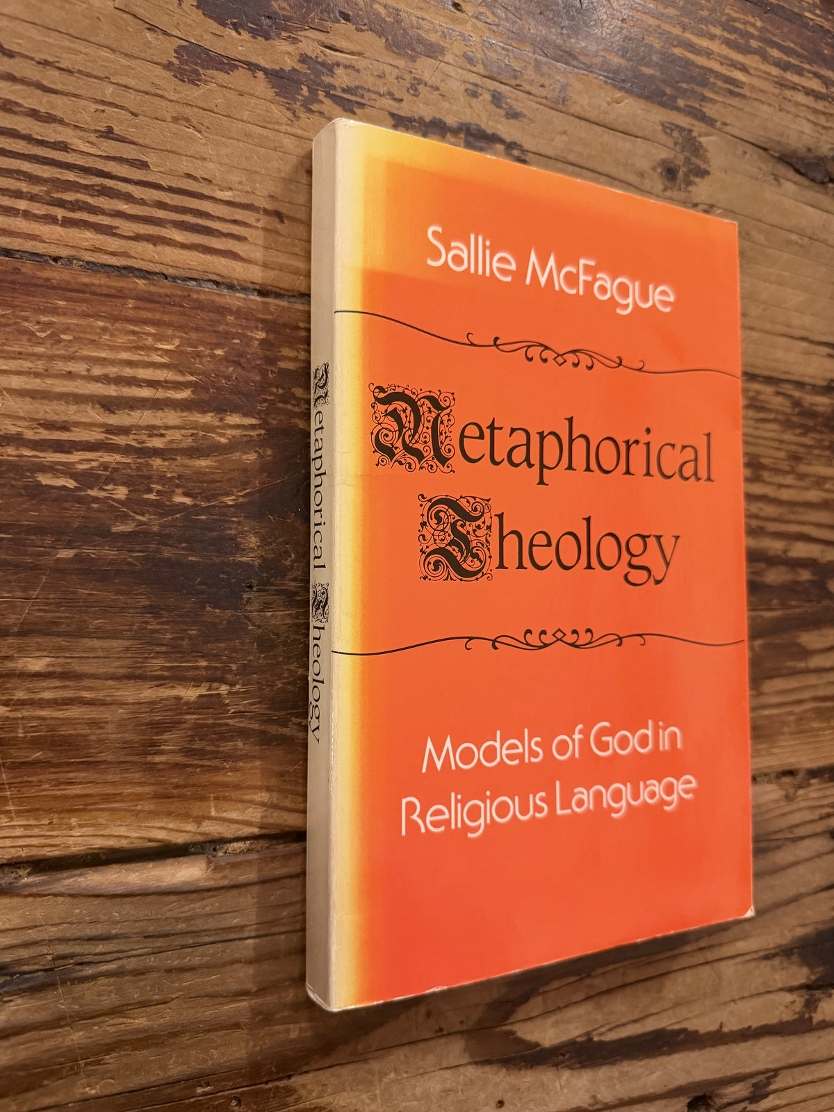 Front cover and spine of a book with the title 'Metaphorical Theology, Models of God in Religious Language' by Sallie McFague, exposed on a wooden surface 