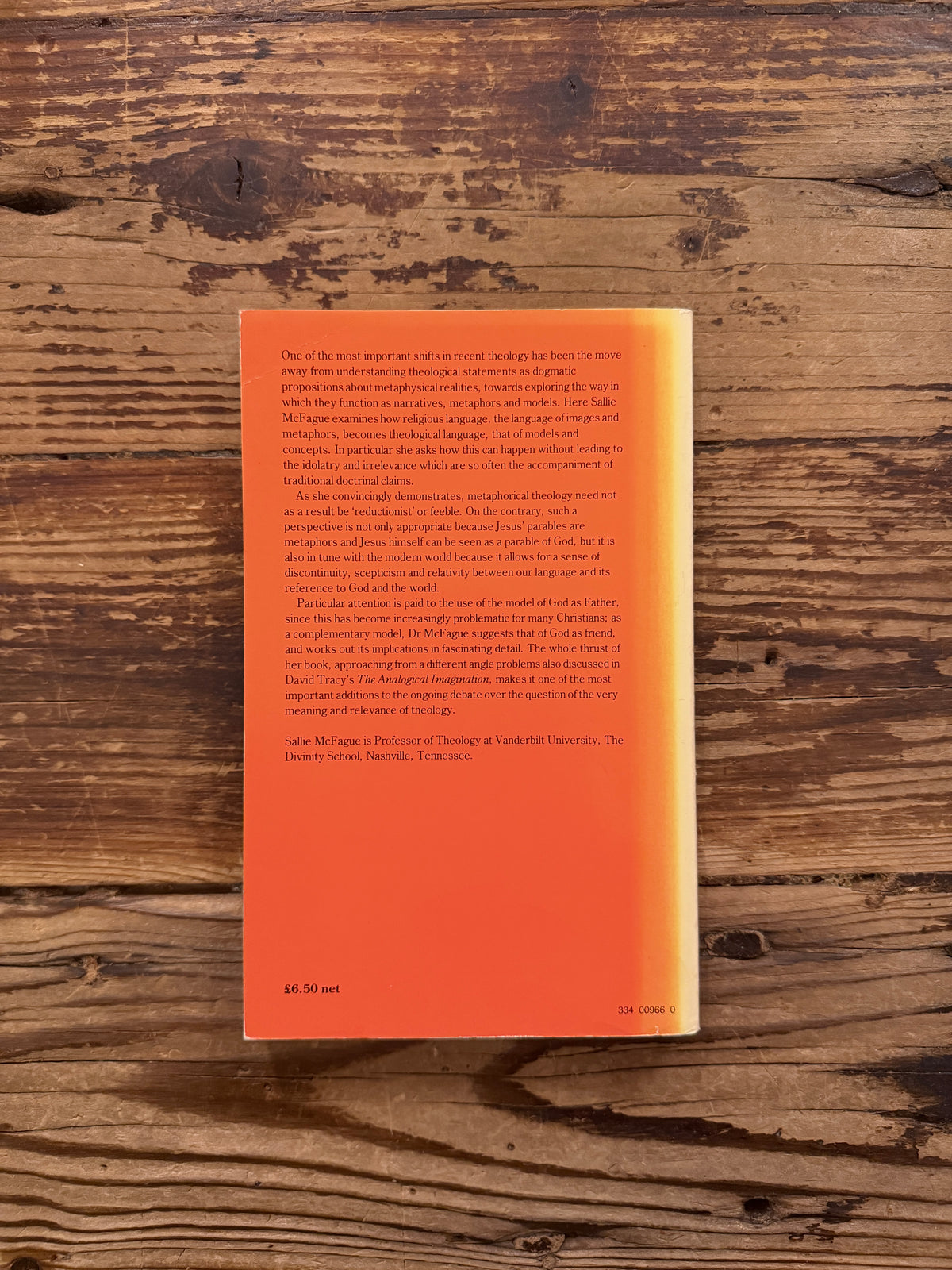Back cover of a book with the title 'Metaphorical Theology, Models of God in Religious Language' by Sallie McFague, exposed on a wooden surface 