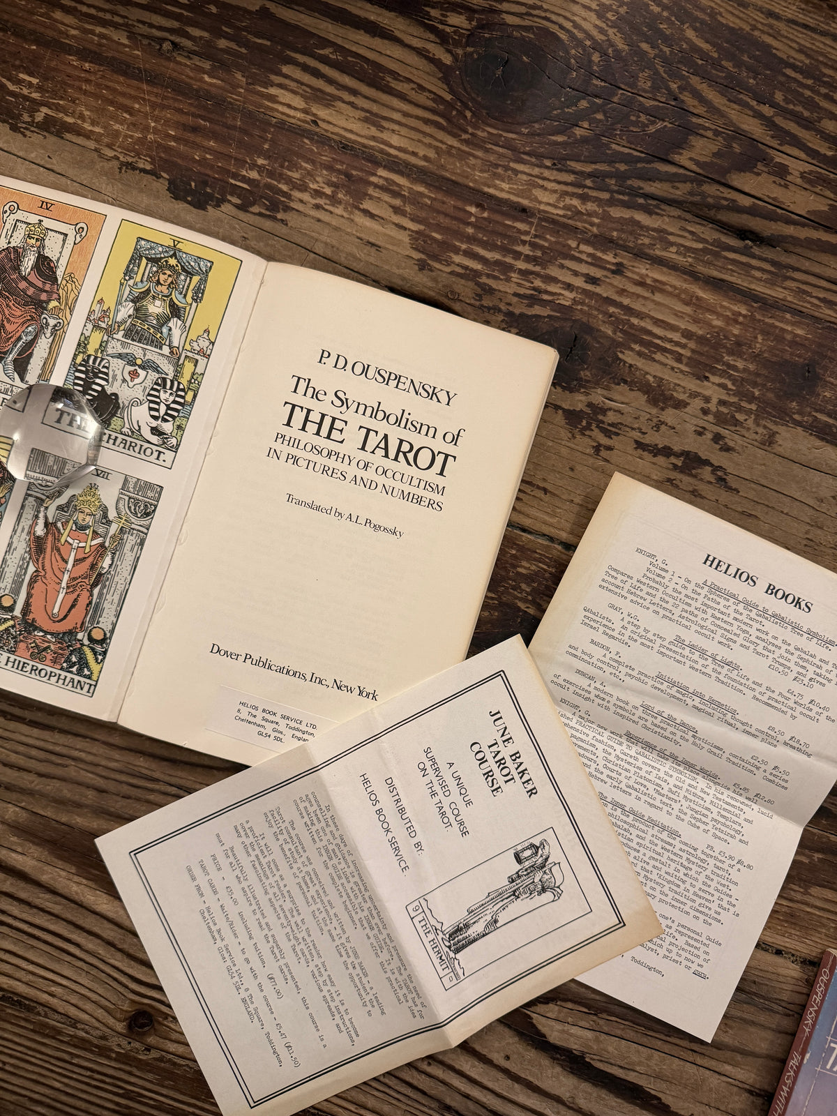 Open book with the title  'The symbolism of the Tarot, philosophy of Occultism in Pictures and Numbers' by P. D. Ouspensky, plus two pages of ephemera from Helios books service ltd lying on a wooden surface