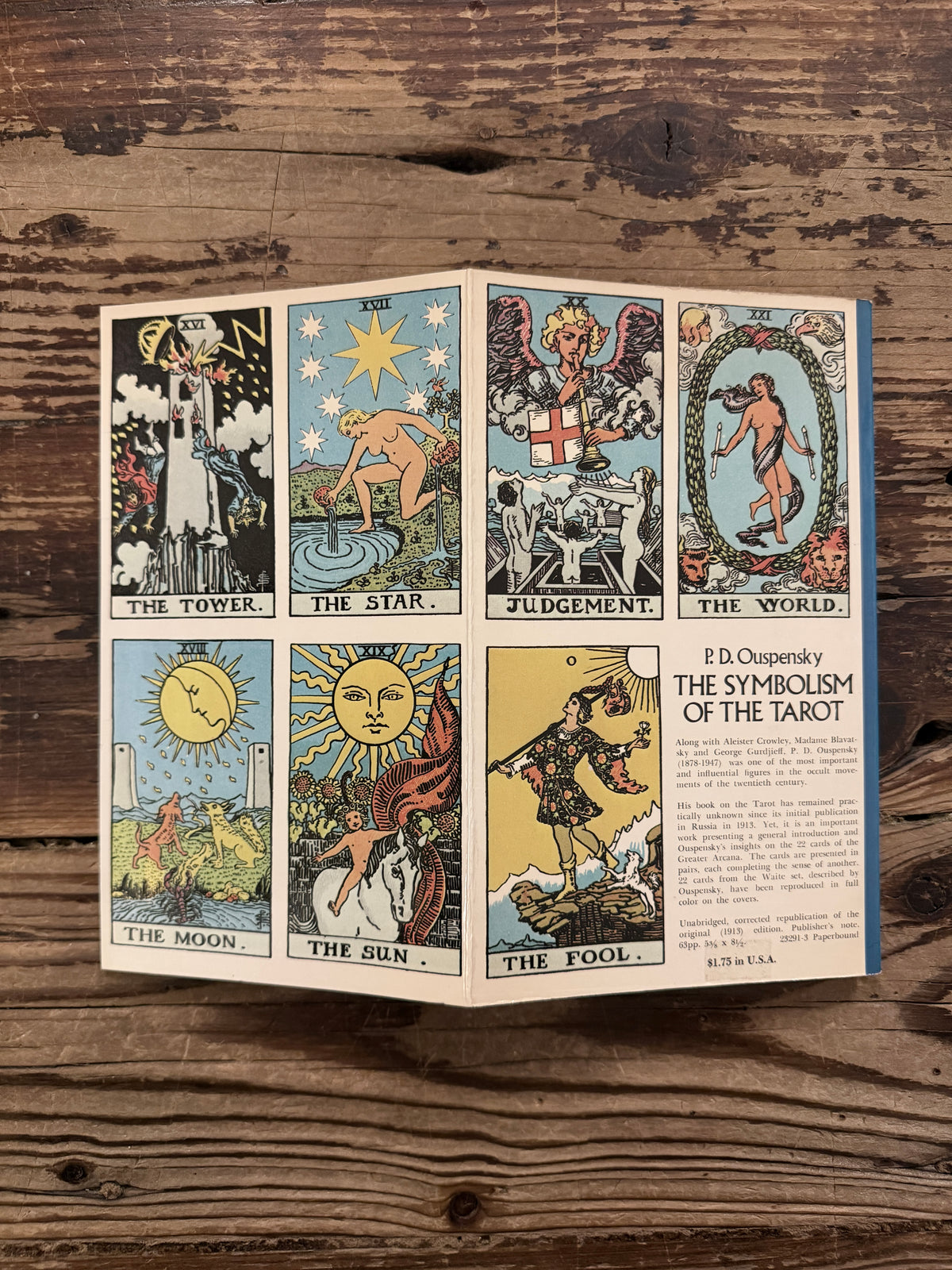 Last page and back cover showing the French Flaps with the tarot illustrations by Waite of a book with the title  'The symbolism of the Tarot, philosophy of Occultism in Pictures and Numbers' by P. D. Ouspensky, lying on a wooden surface