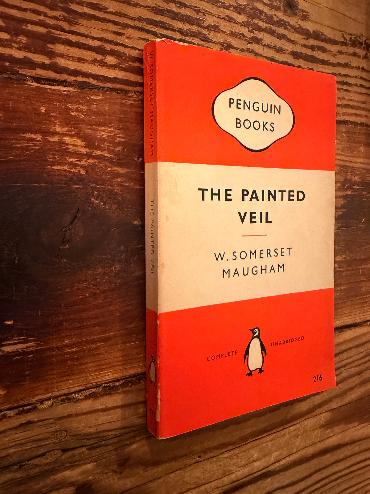 Front cover and spine of a book with the title 'The Painted veil' by W. Somerset Maugham, Penguin Books n. 872, reprint 1959, lying on a wooden surface