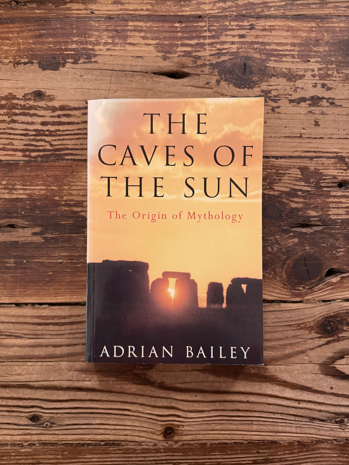 Front cover of book titled 'The Caves of the Sun: The Origin of Mythology' by Adrian Bailey, lying on a wooden surface