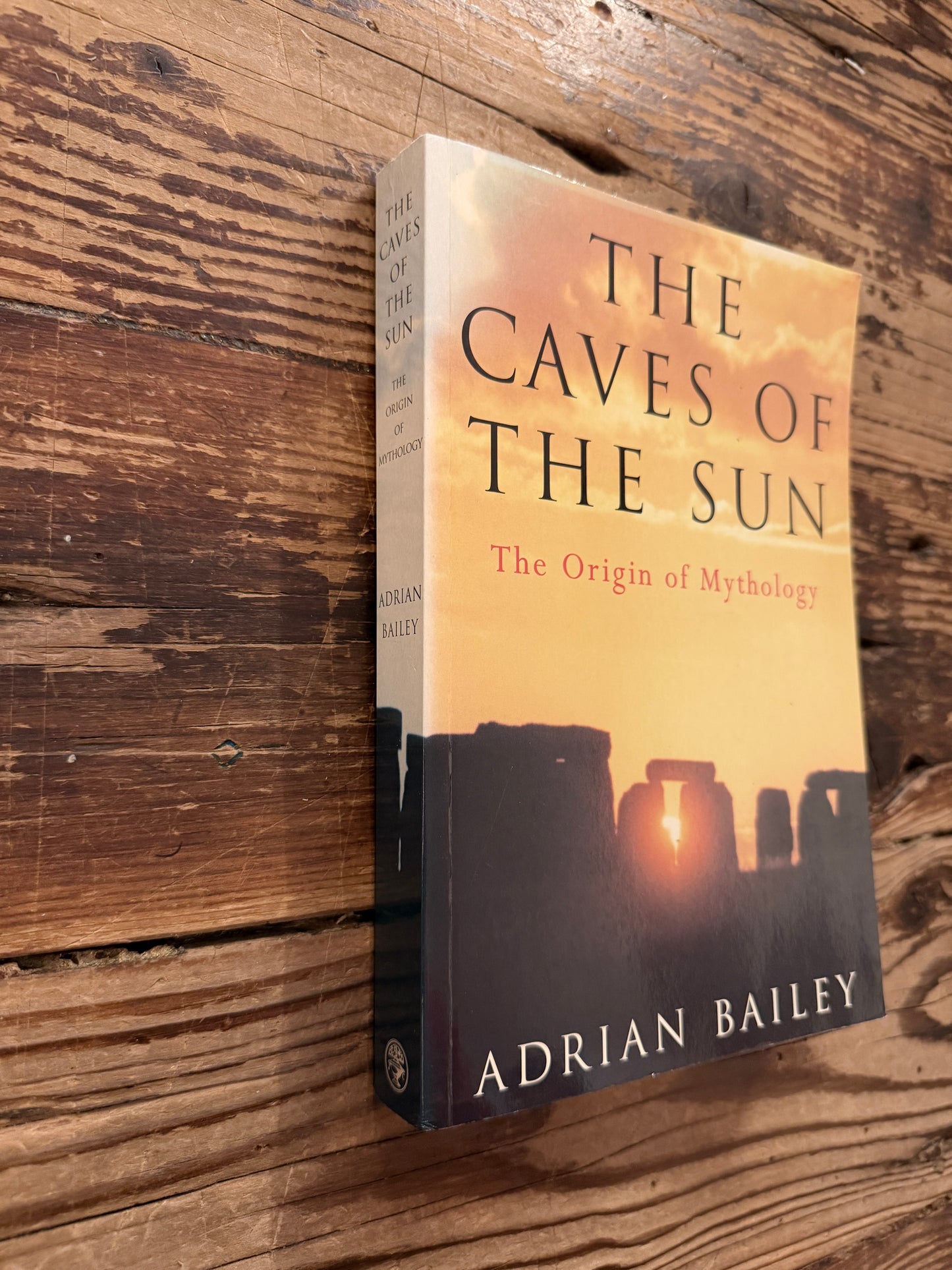 Front cover and spine of book titled 'The Caves of the Sun: The Origin of Mythology' by Adrian Bailey, lying on a wooden surface