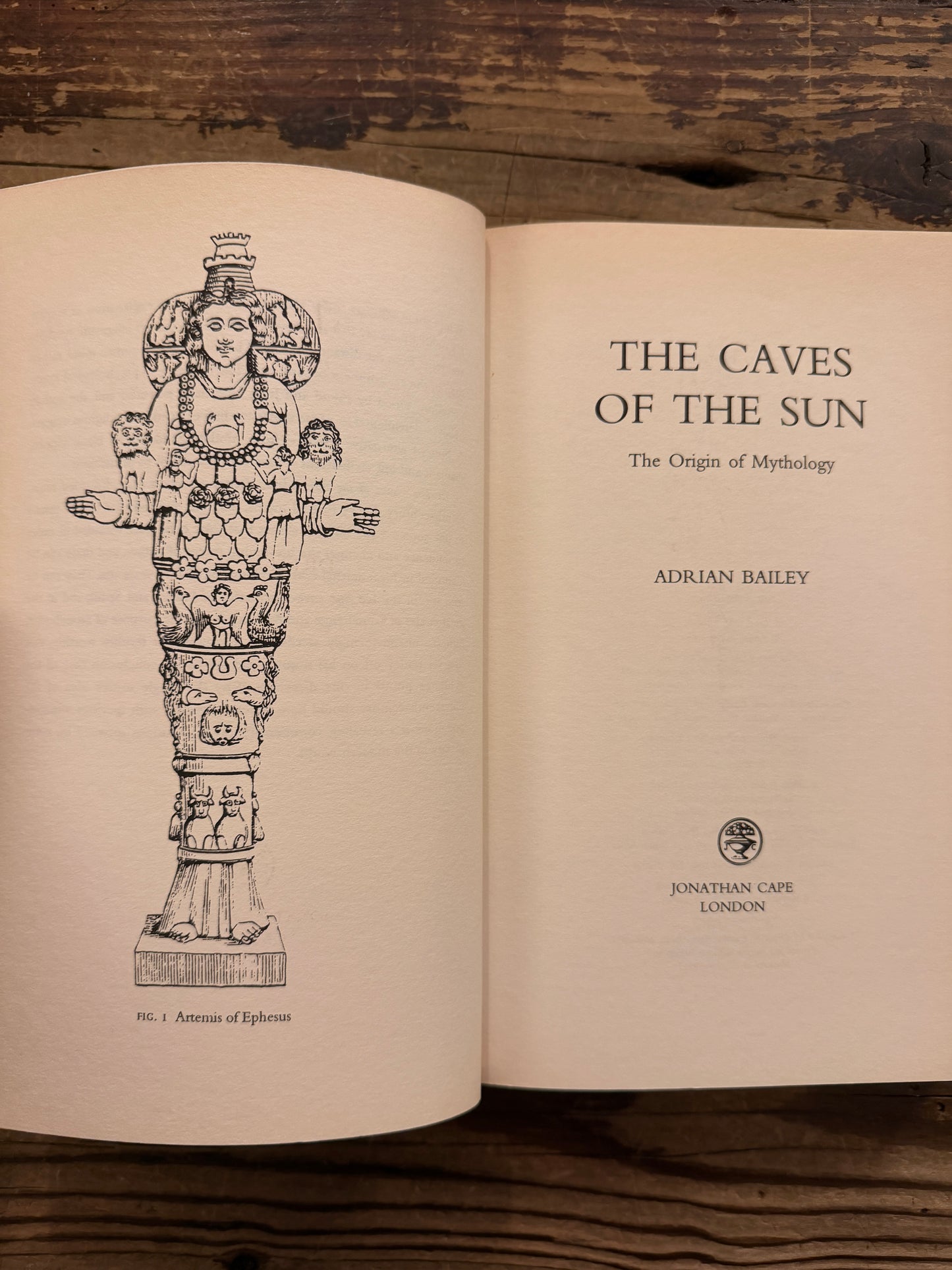 Open book titled 'The Caves of the Sun: The Origin of Mythology' by Adrian Bailey, lying on a wooden surface